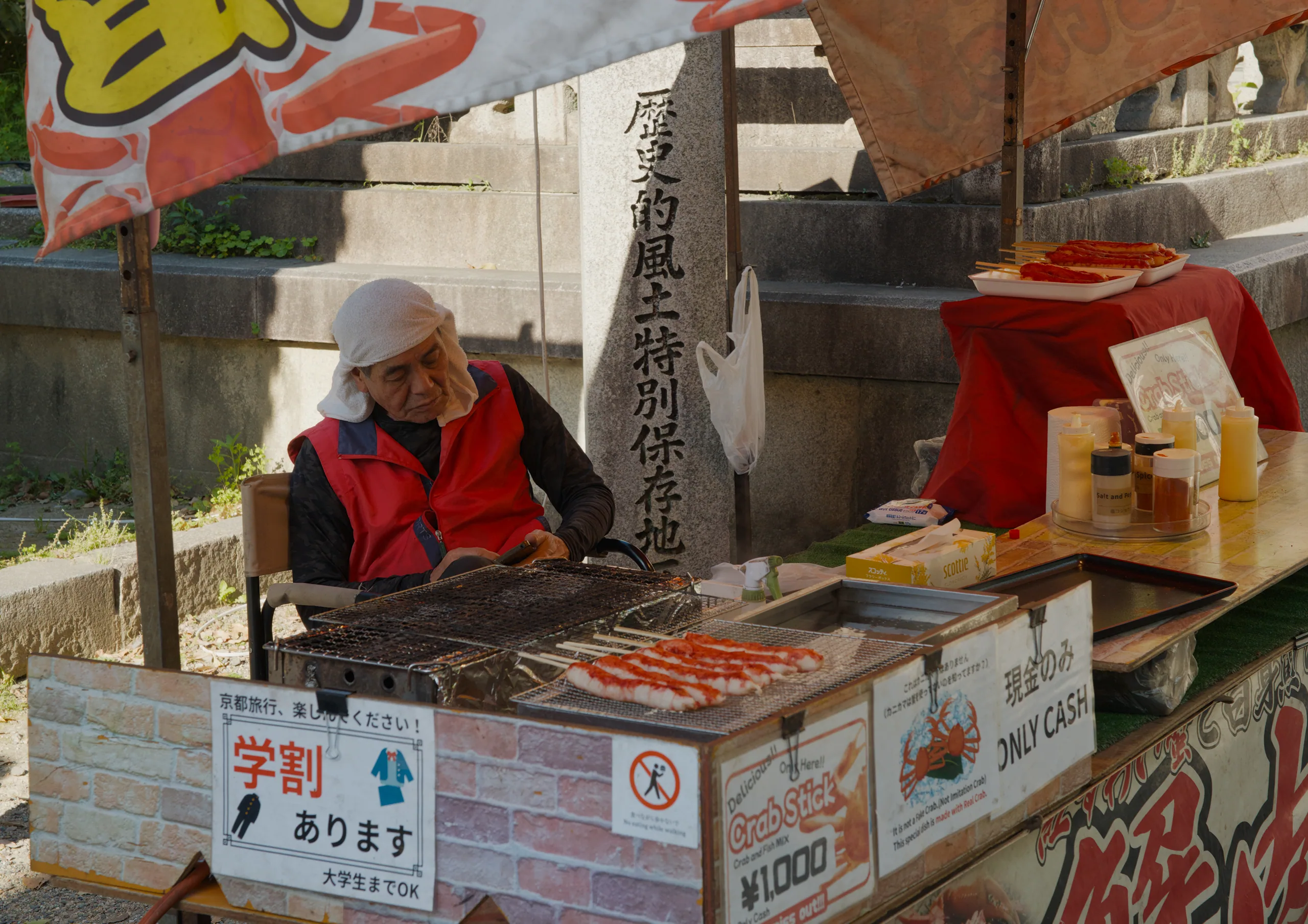 Vendor in red jacket preparing takoyaki at a street food stall with Japanese signage overhead.