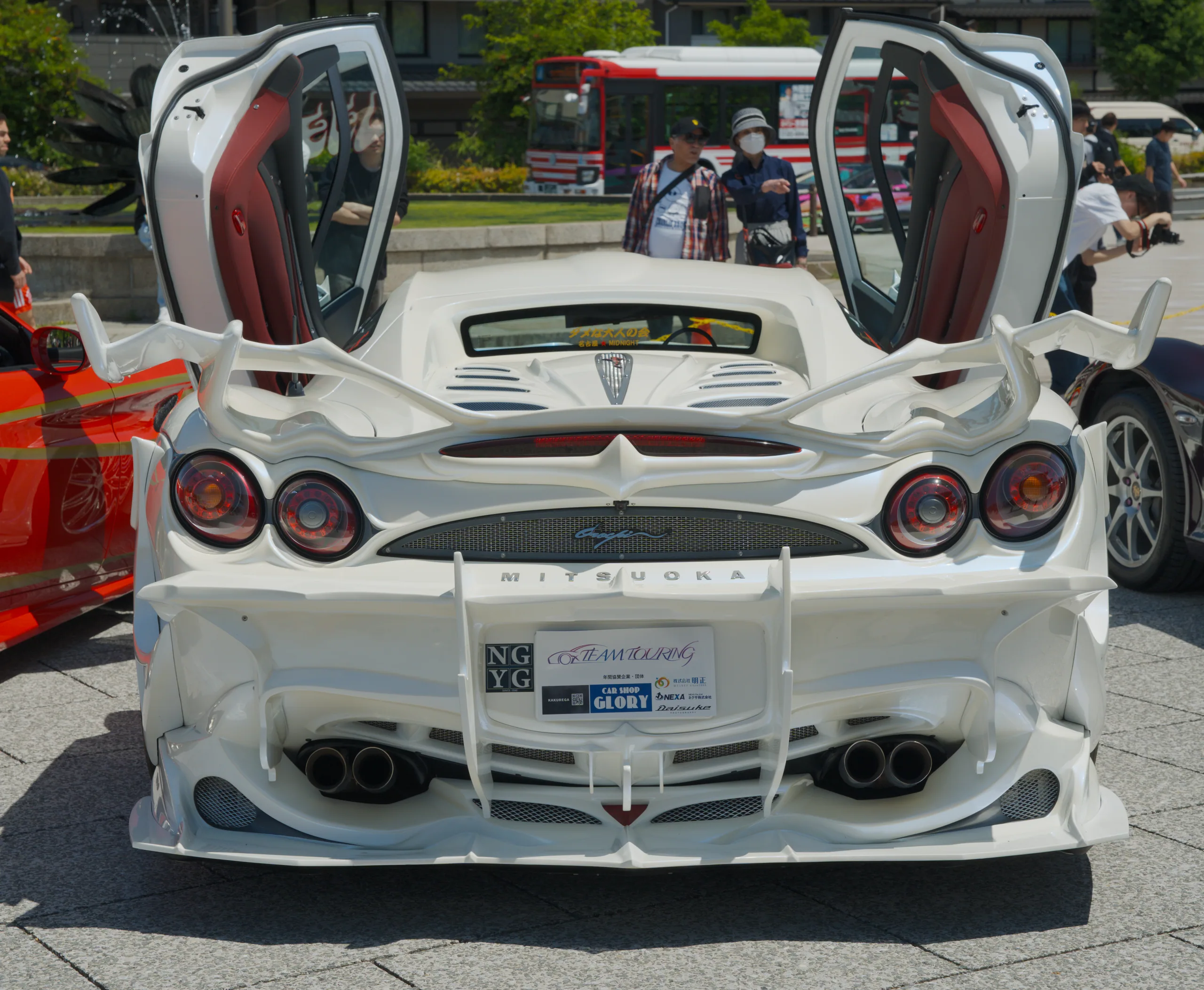 A white Pagani supercar with gull-wing doors open, displayed at a car show.