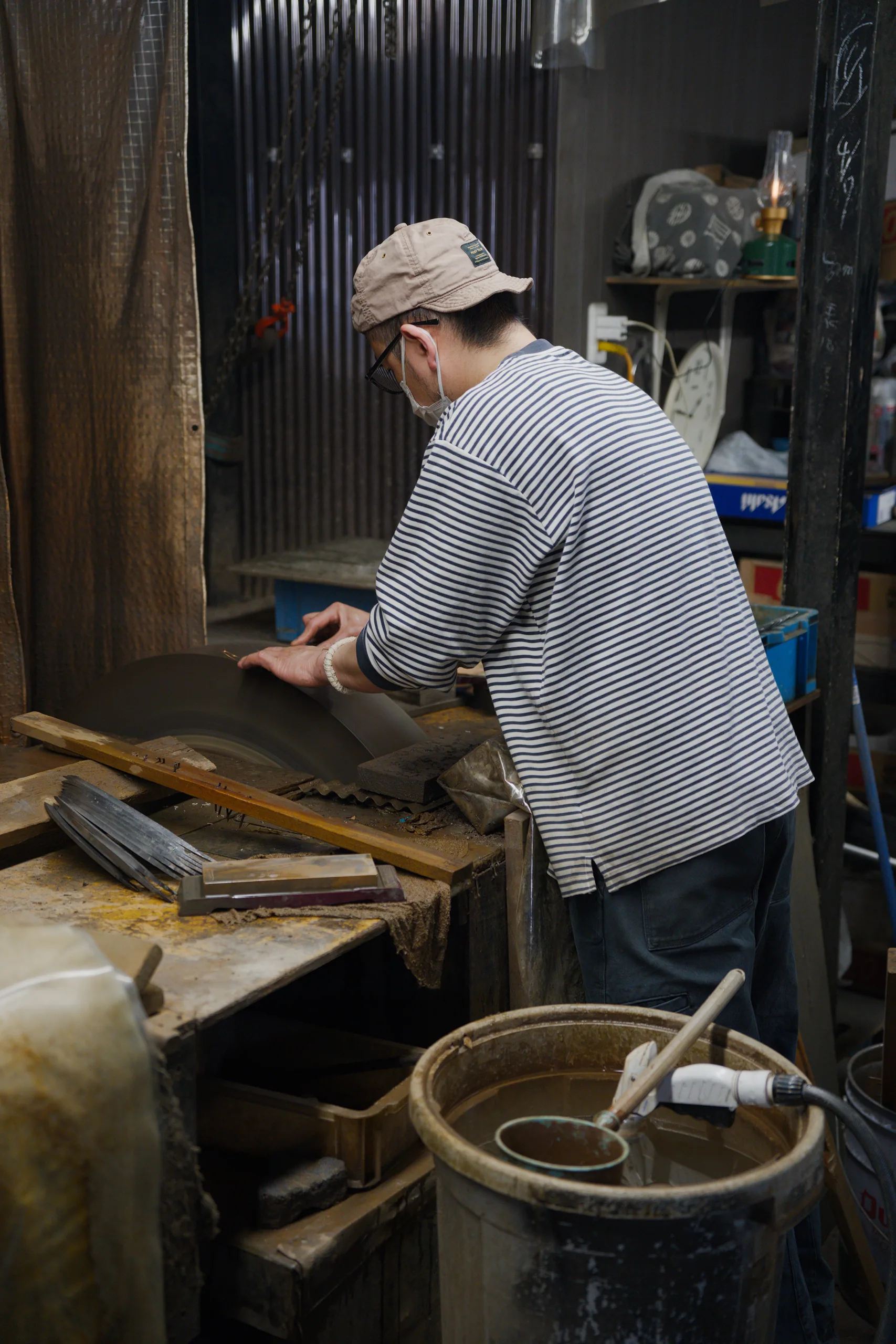 A person in a striped shirt works with wood and hand tools in a workshop.