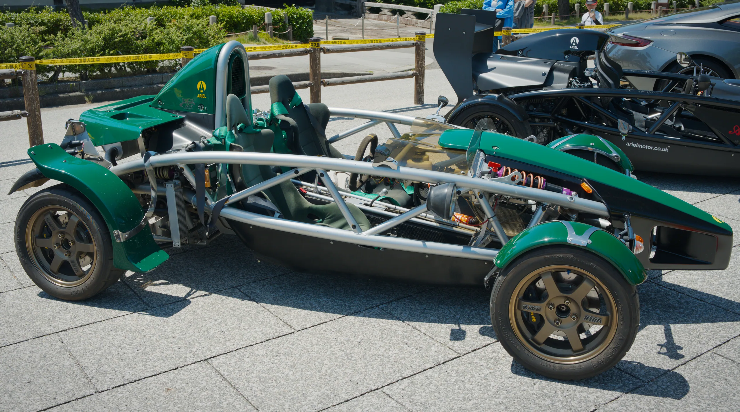 A green sports car with an exposed steel frame chassis displayed at a car show.