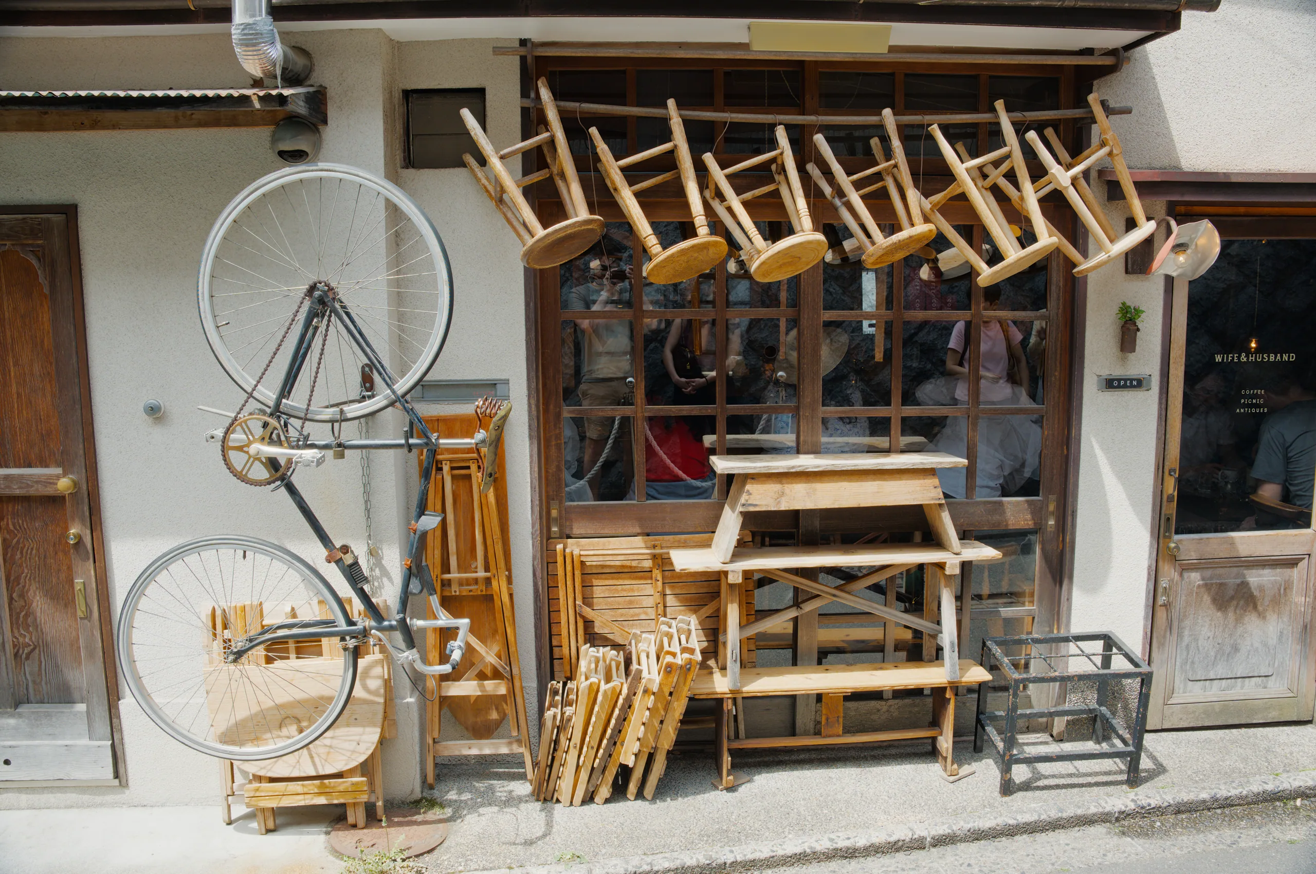 A street-level antique shop displaying wooden furniture, bicycles, and decorative items under a wooden frame overhang.