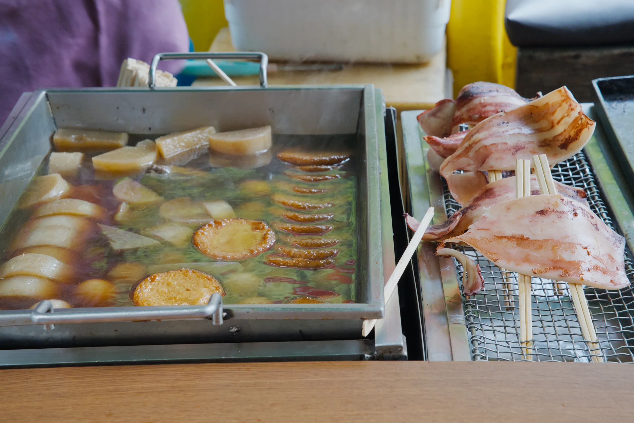 Pieces of grilled meat char on a charcoal fire next to bottles of sake.
