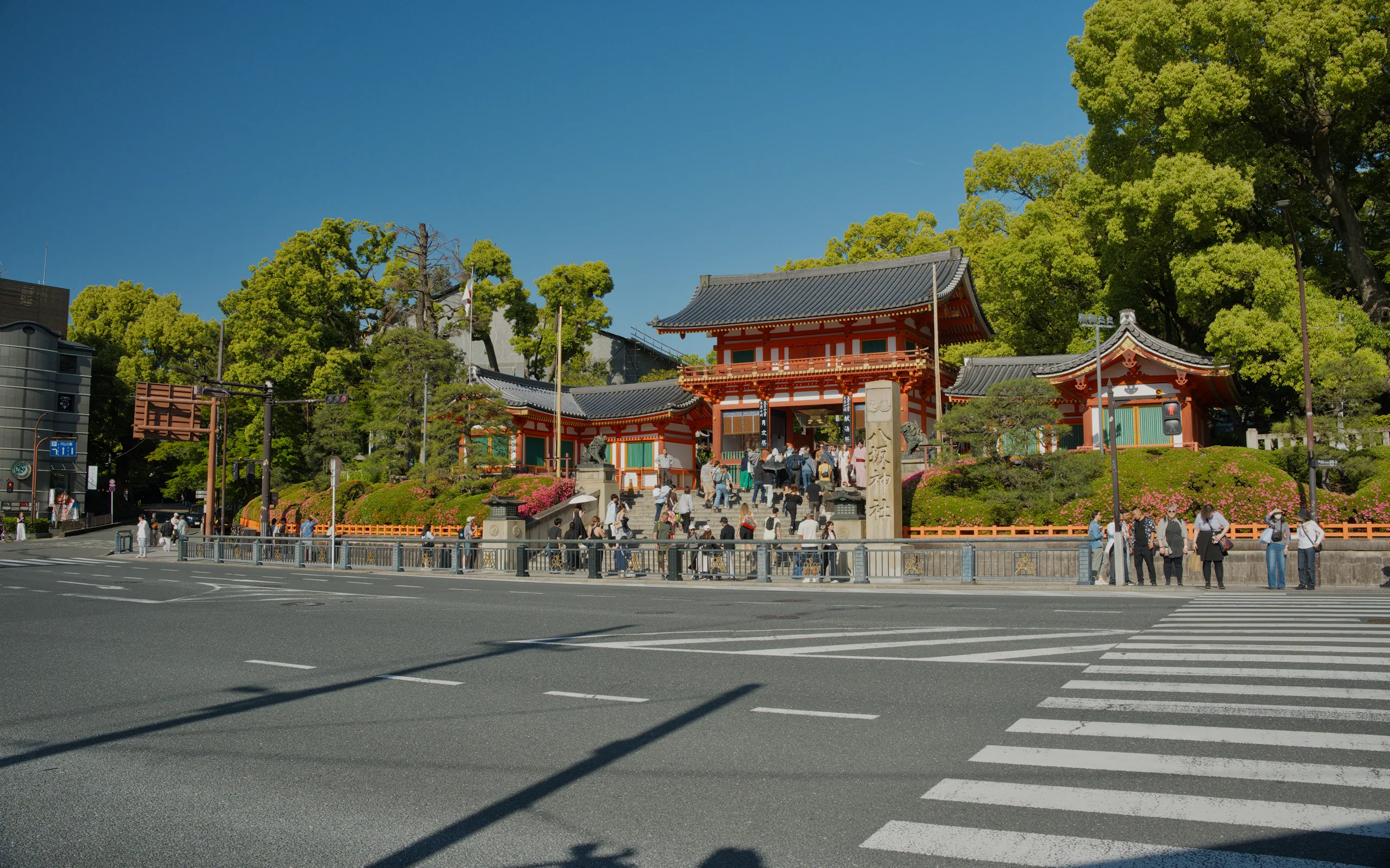 A large red Japanese temple gate viewed from a sunlit plaza with pedestrians in front.