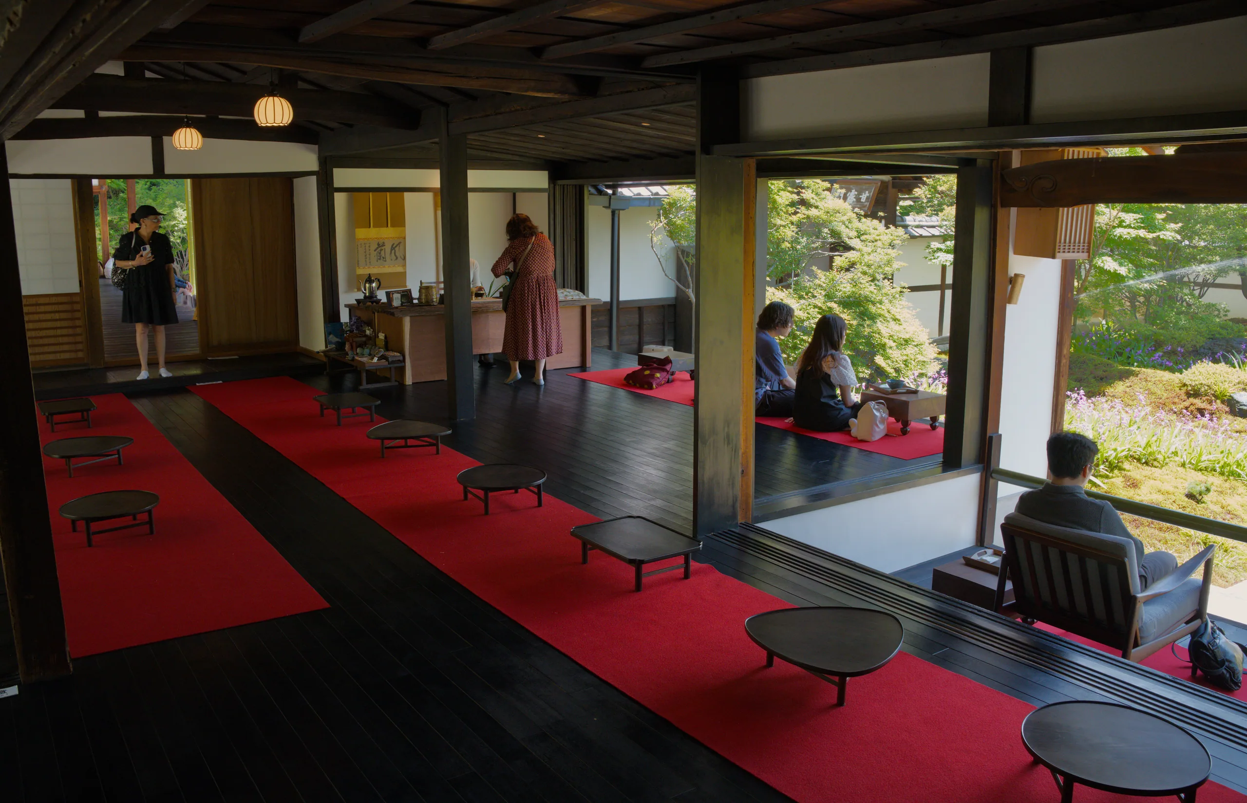 The red-carpeted interior gallery of a traditional building with exposed wooden beams, open on all sides to manicured gardens.
