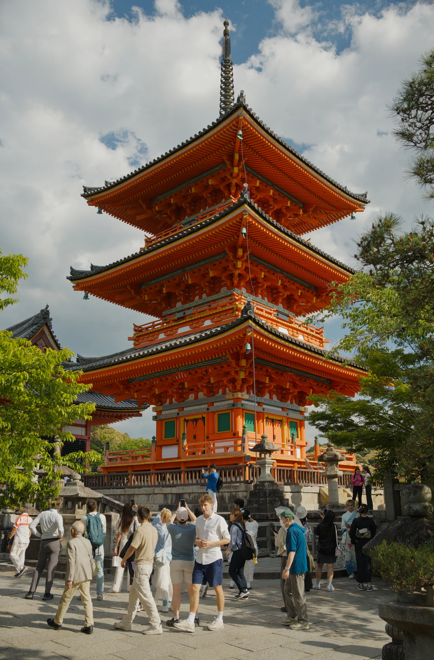 A five-tiered red pagoda rises above a plaza full of visitors on a partly cloudy day.