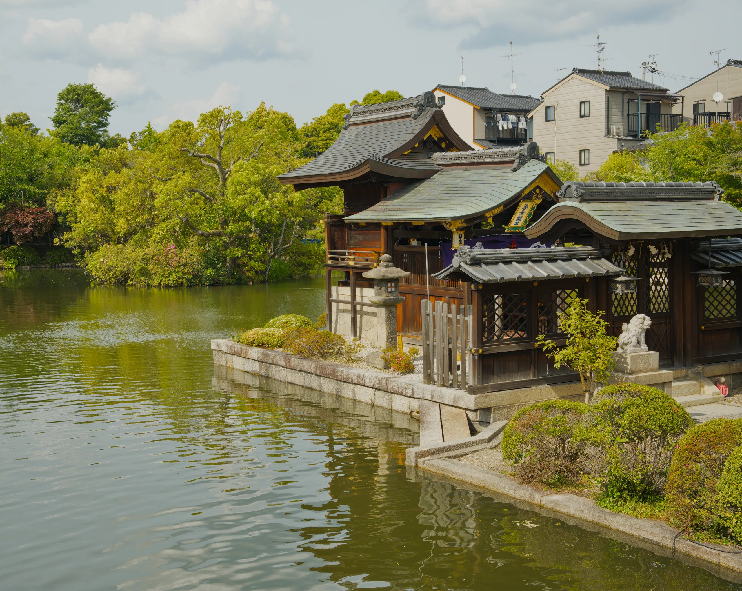 A wooden building with layered rooflines reflected in still water, with stone lanterns nearby.