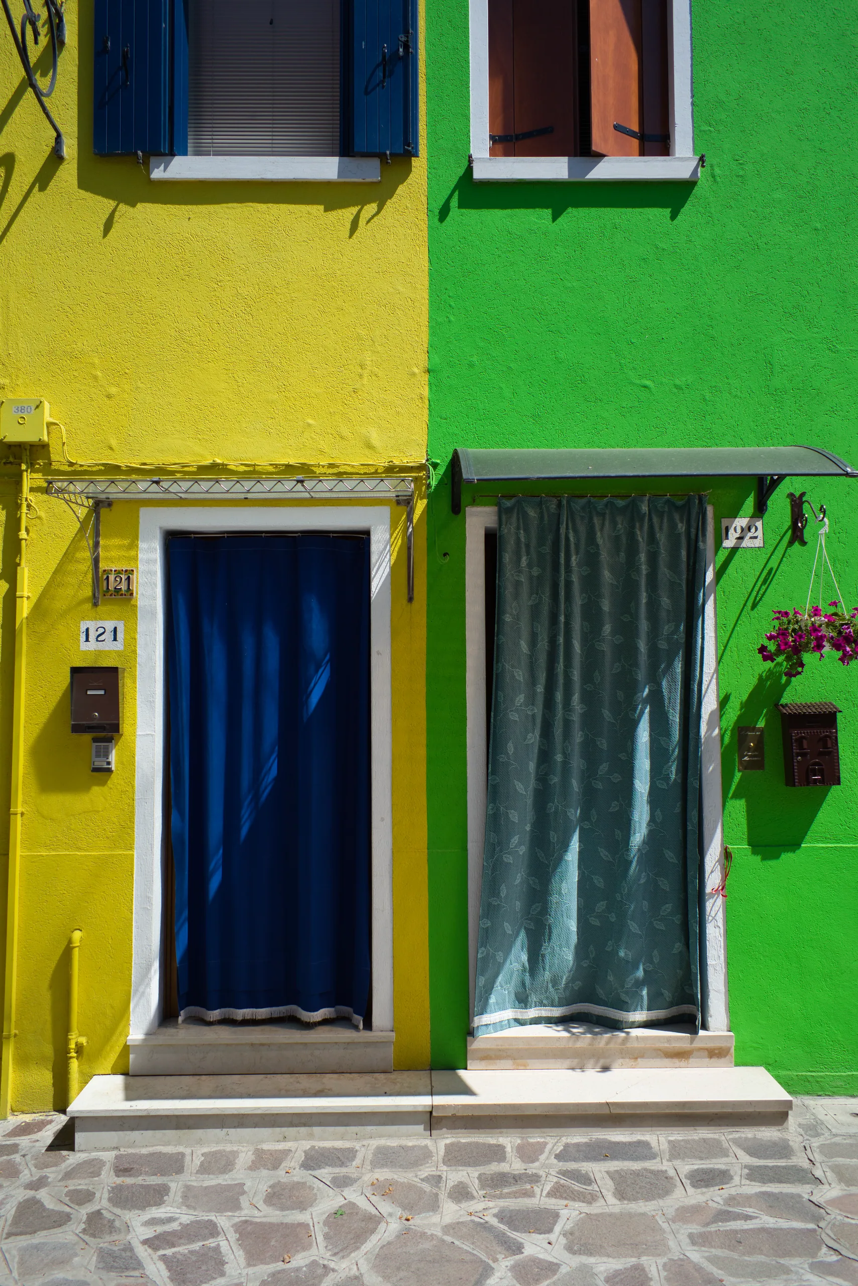 A bright yellow house front meeting a green one, a blue curtain hanging in the yellow doorway.
