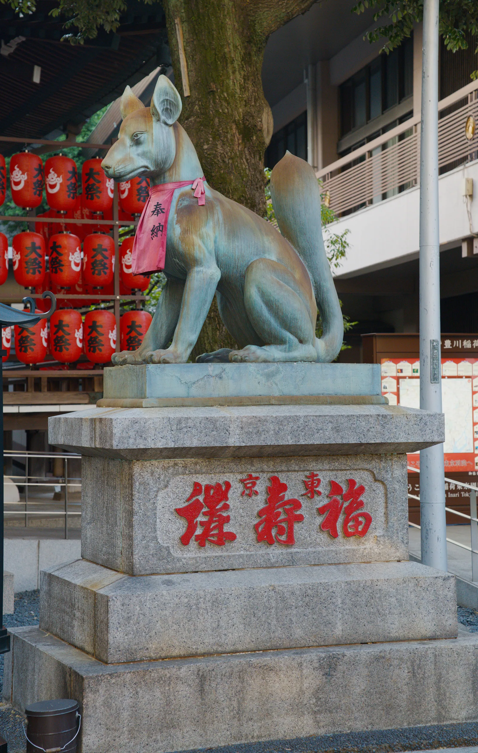 A stone fox statue at a shrine entrance with red lanterns in the background.