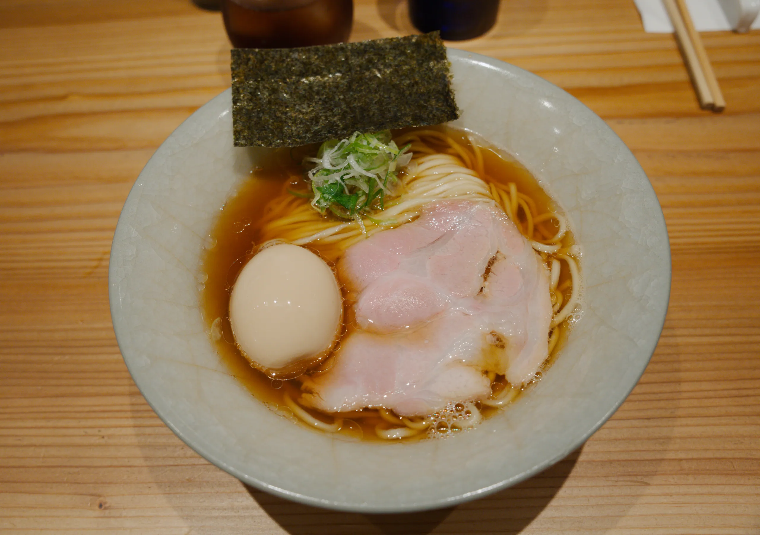 A bowl of ramen topped with a soft-boiled egg, sliced pork, and seaweed on a wooden counter.