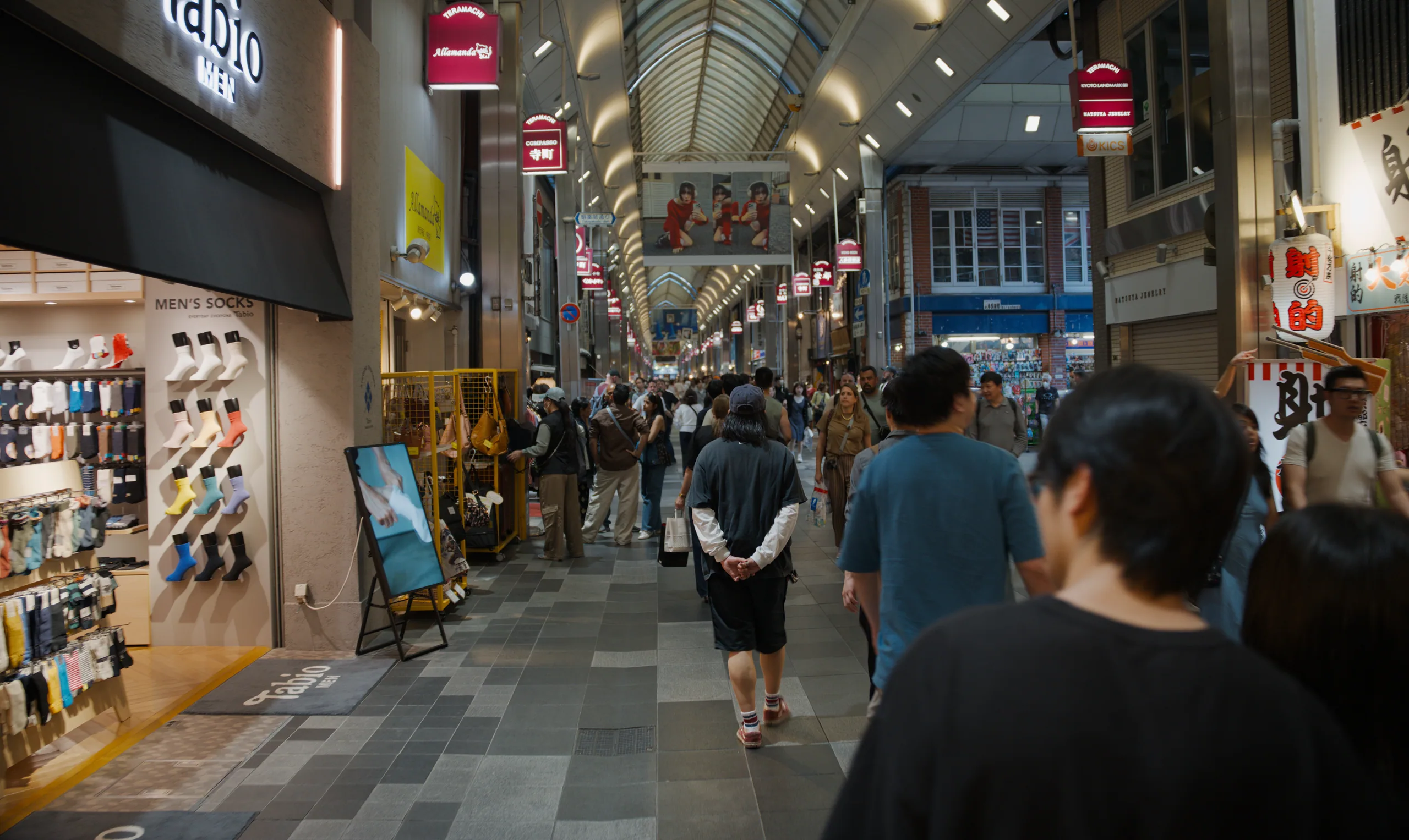 Covered arcade crowded with pedestrians at night, storefronts lit by neon signs.
