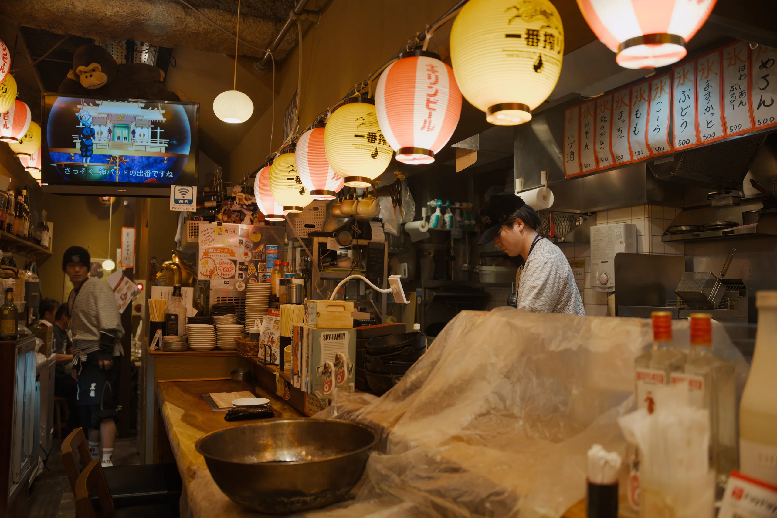 Restaurant seating area with hanging paper lanterns illuminating a white counter where customers are seated.