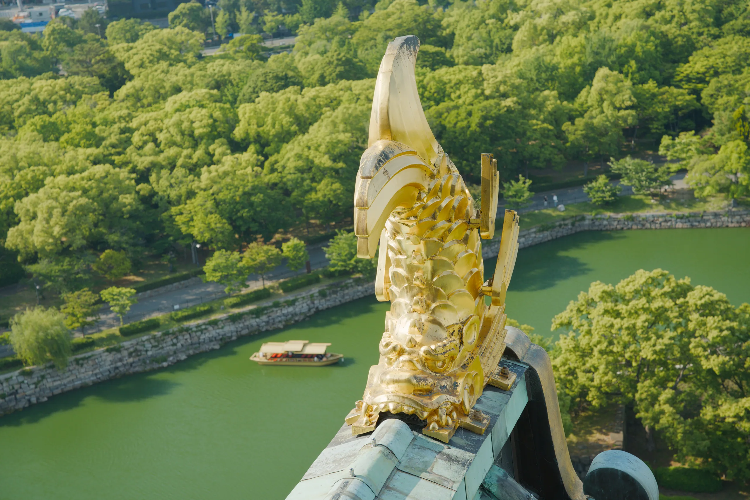 Golden finial from a castle roof rises above a river lined with dense green forest.