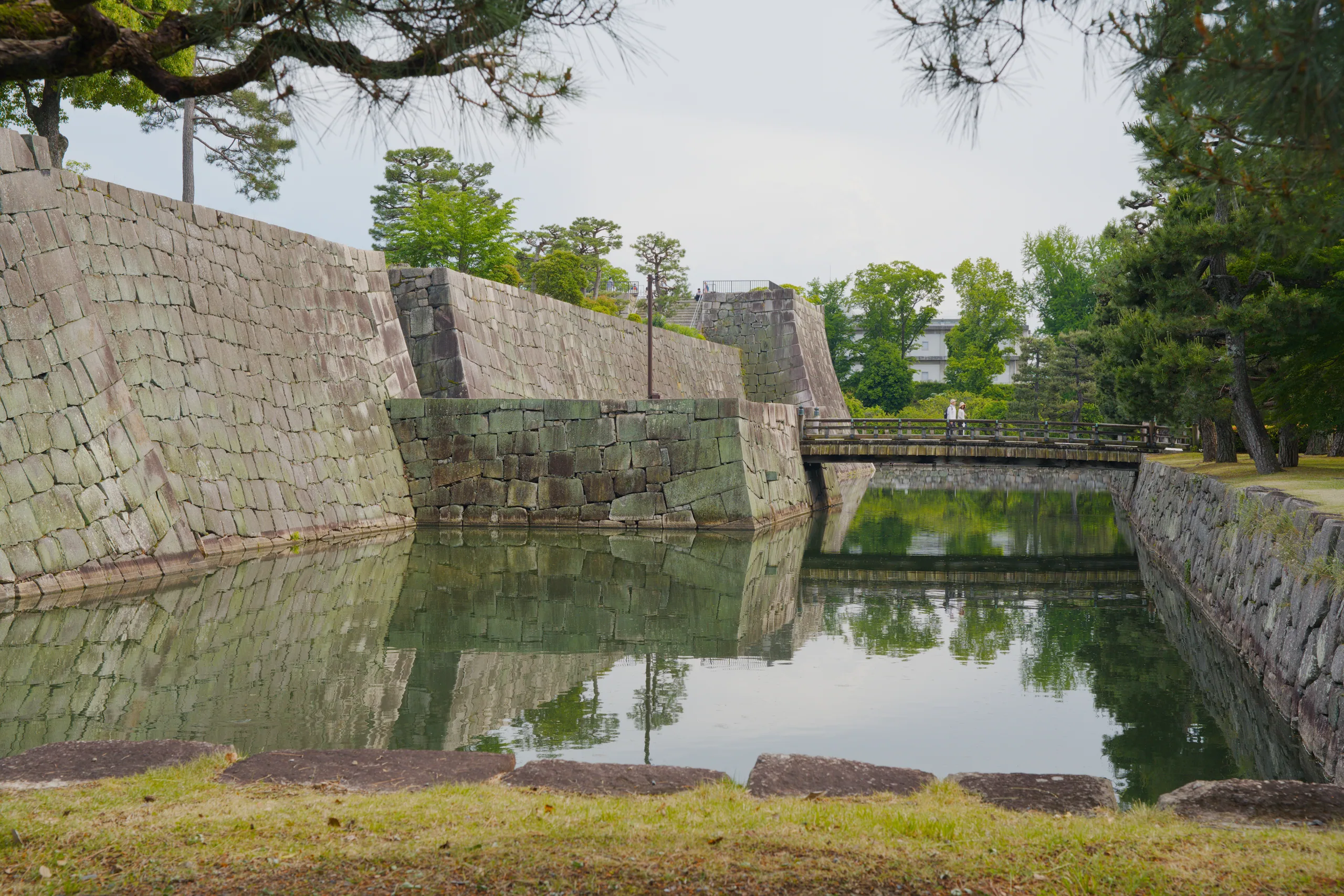 Stone castle walls angle across a still moat and reflect in the water below.