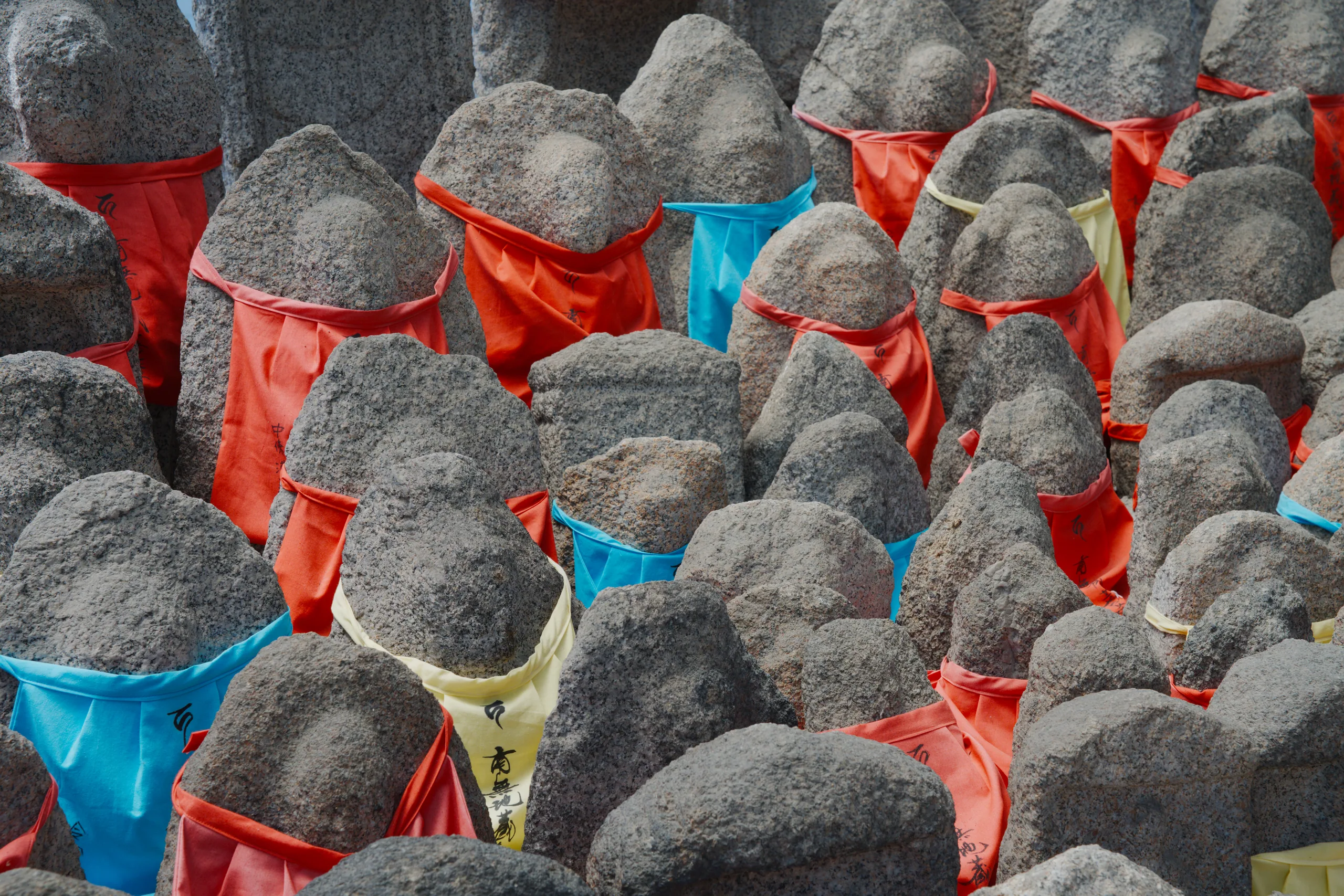 Rows of large gray stone spheres with colorful fabric wrappings in red, blue, and yellow.