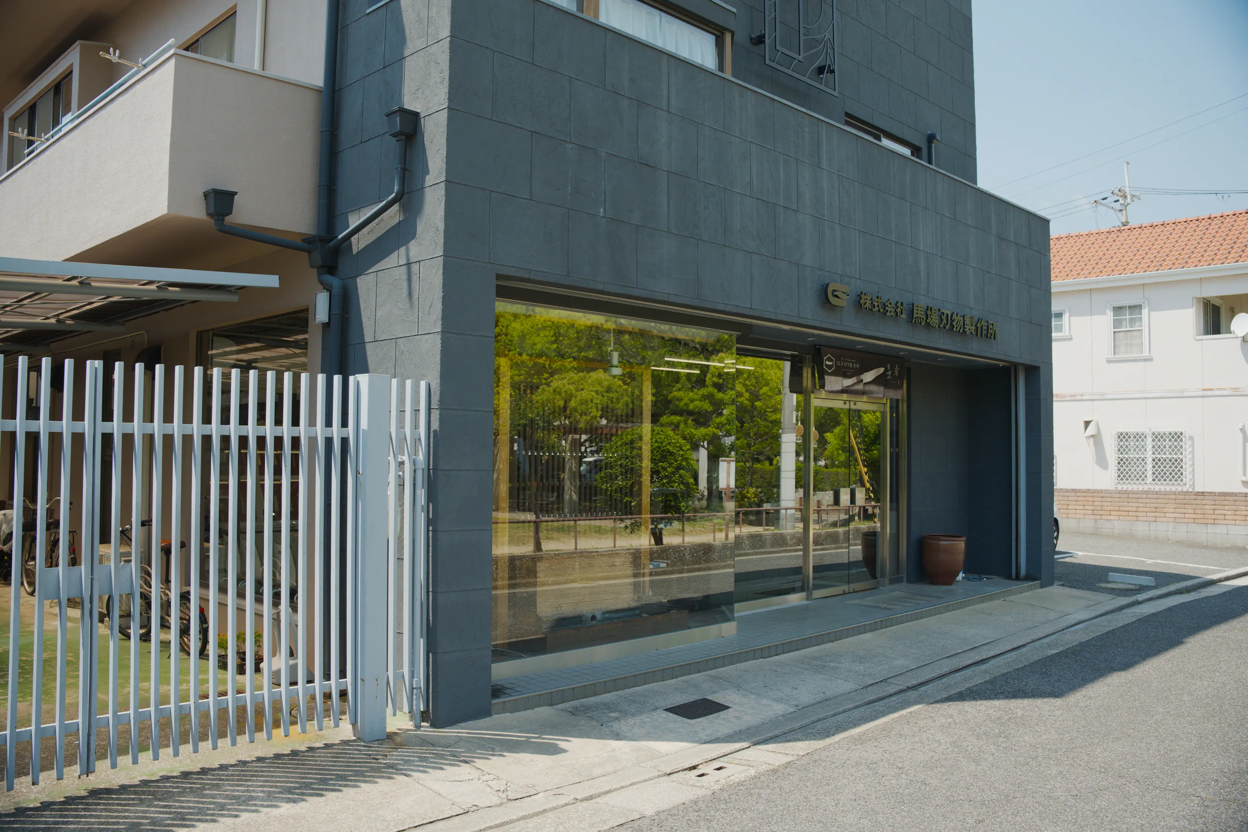 A shopfront with a closed metal shutter beside residential buildings on a quiet street.