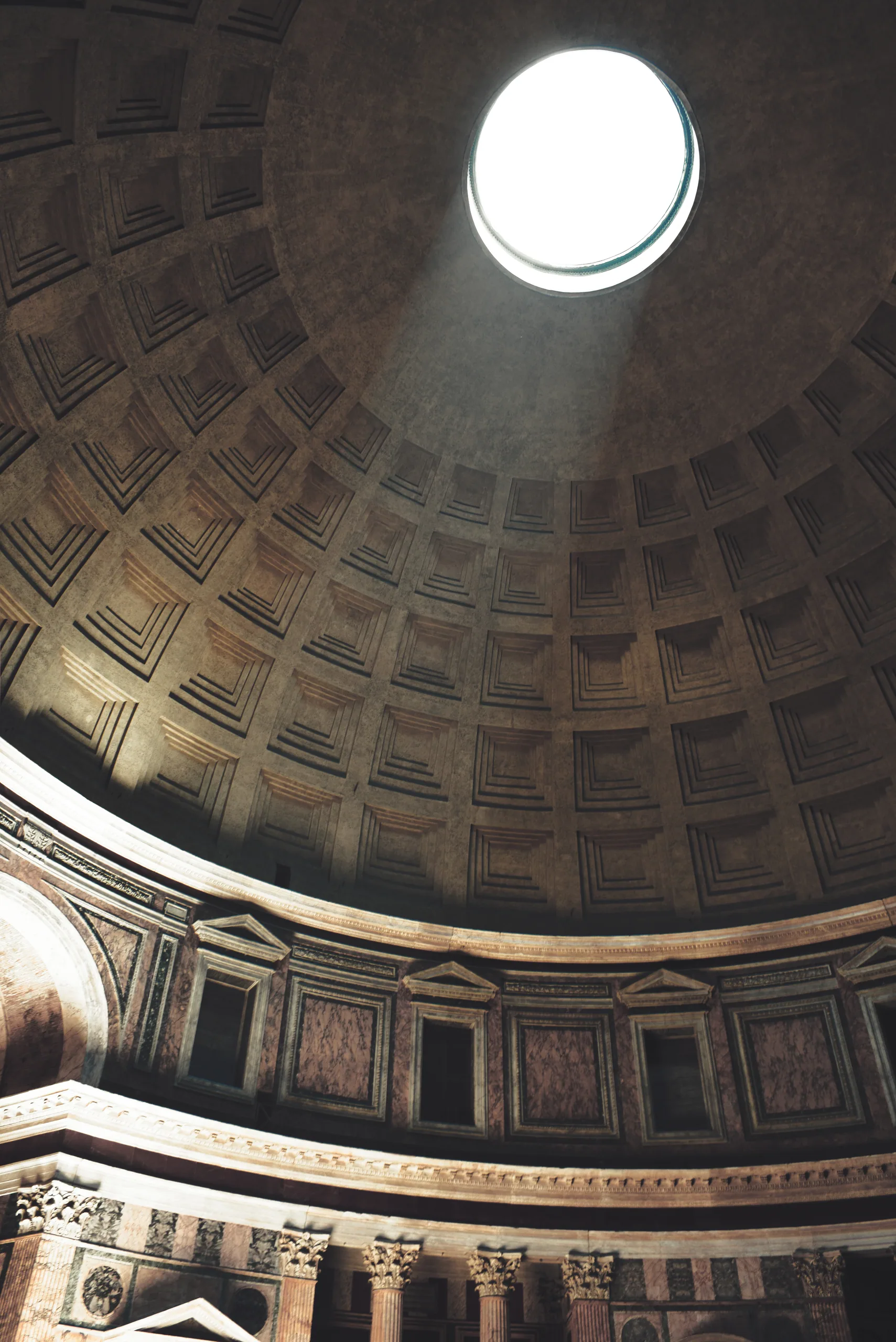 The coffered dome of the Pantheon with a shaft of sunlight coming through the open oculus.