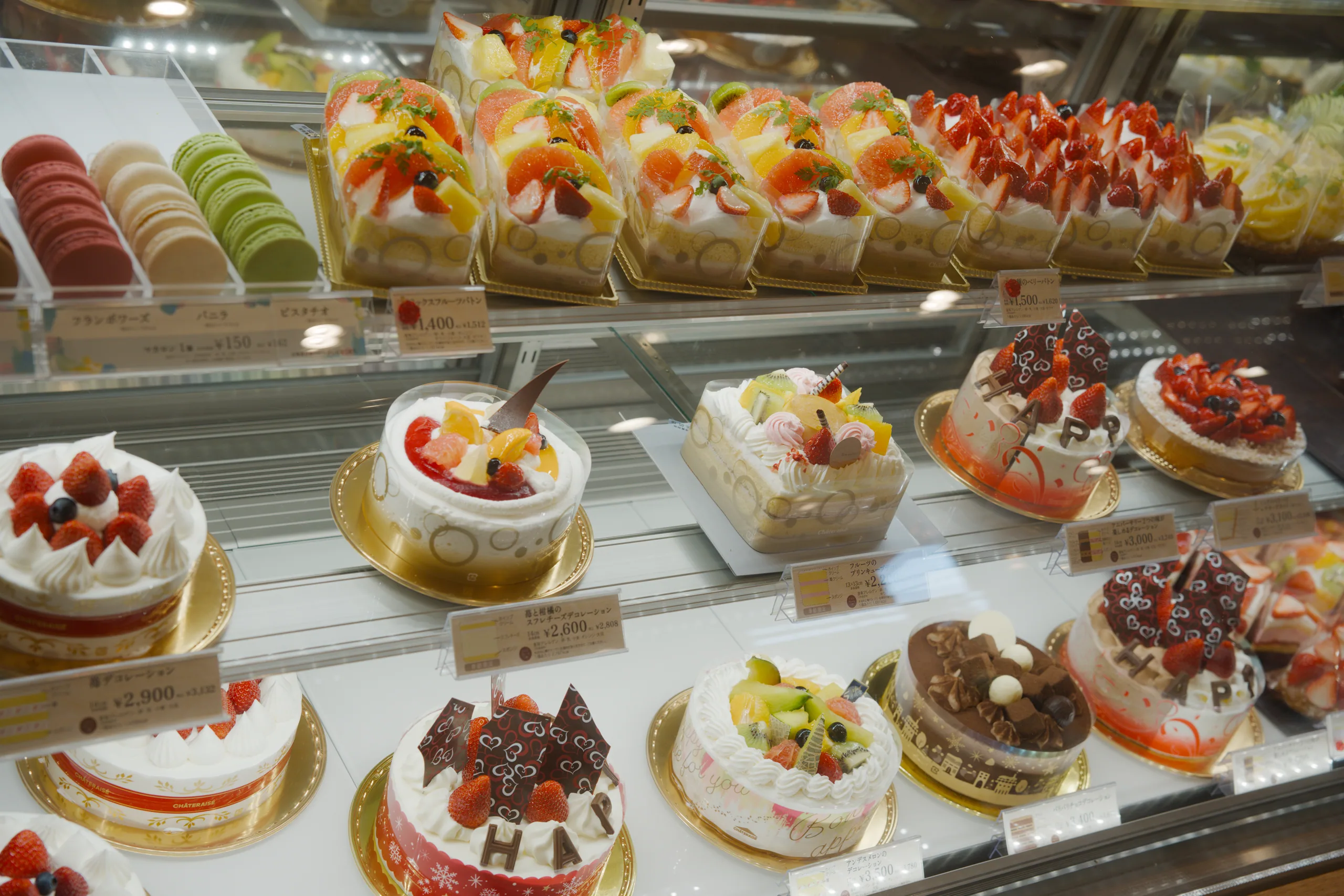 Bakery display case with rows of strawberry-topped pastries and cream cakes.