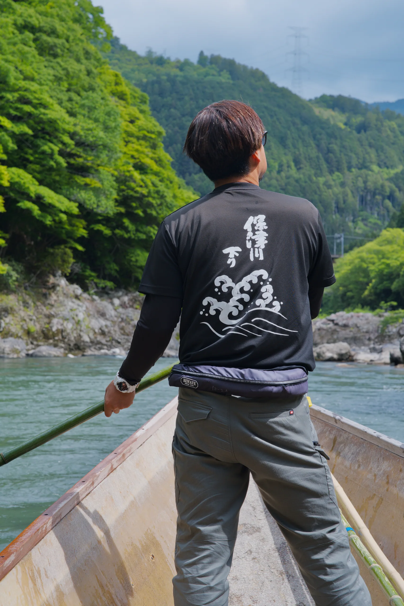 A boatman poles through turquoise water with steep forested banks behind.