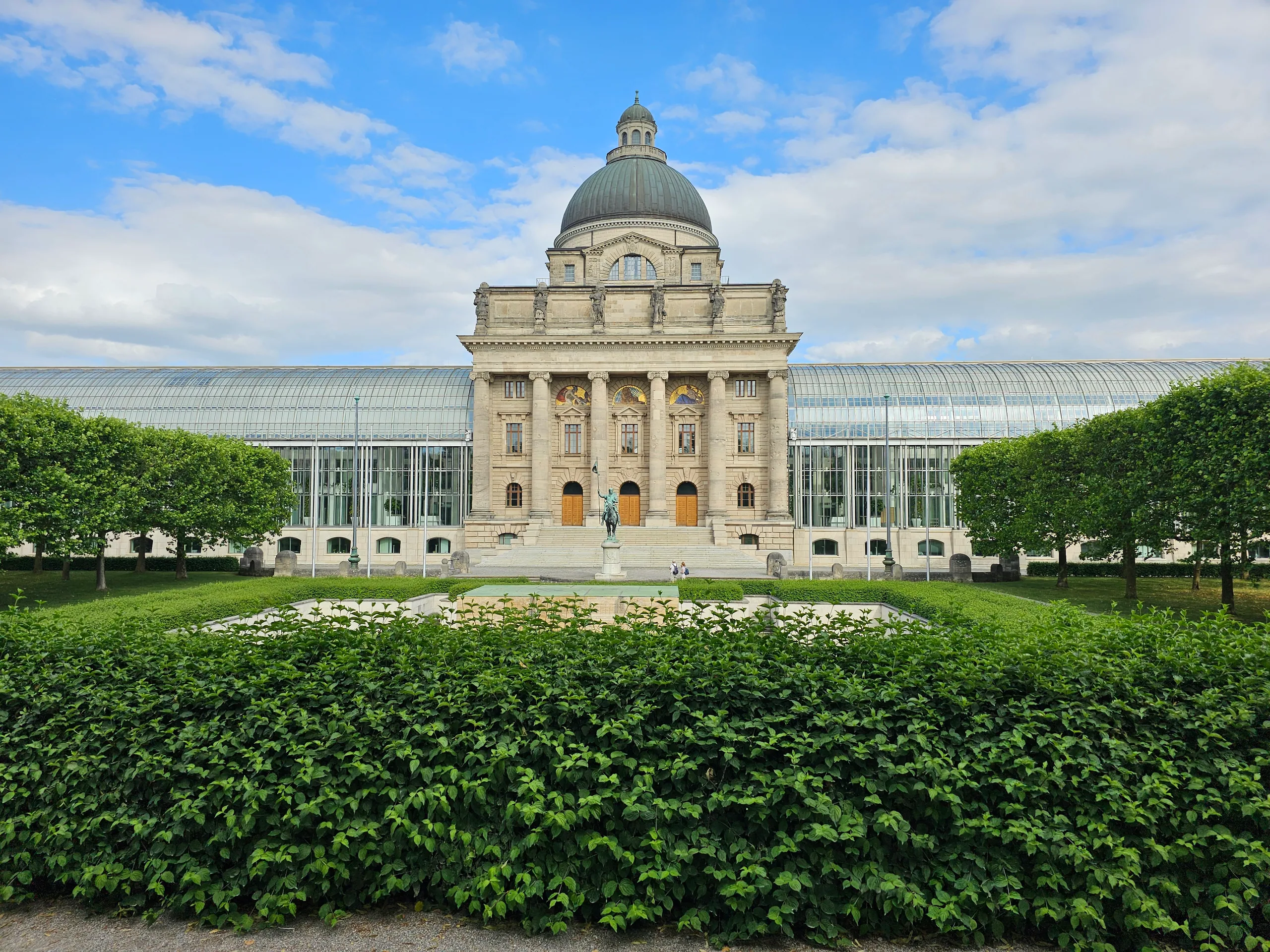 The Bavarian State Chancellery, its glass wings either side of a domed stone centre, above formal hedges and a lily pond.