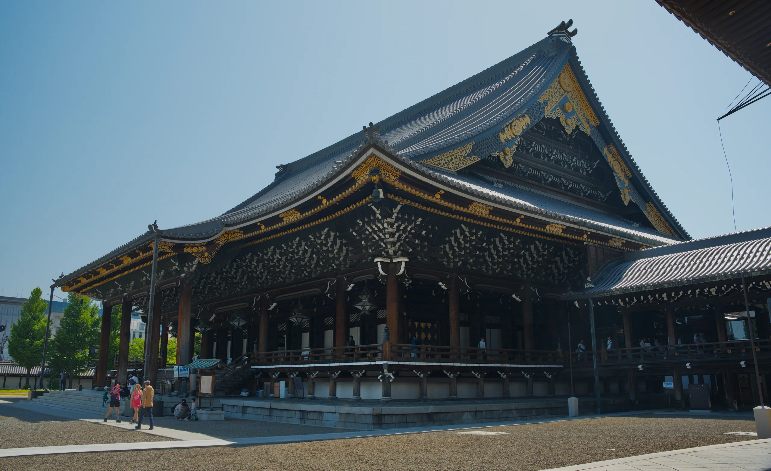 Wooden Buddhist temple with gold-trimmed upturned roofs and visitors in the courtyard.