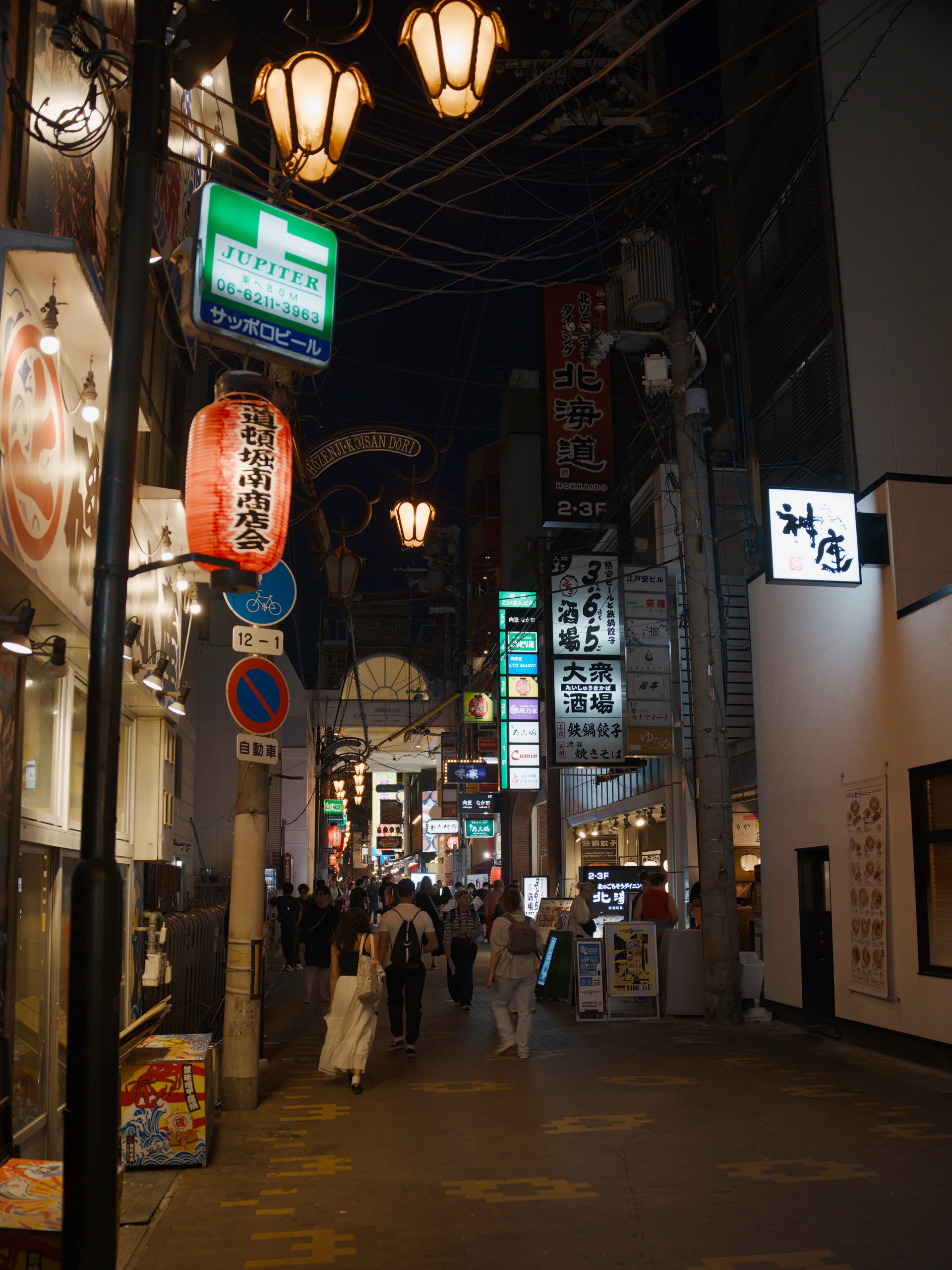 Japanese shopping arcade at night with lanterns and neon signs lining a covered passageway.