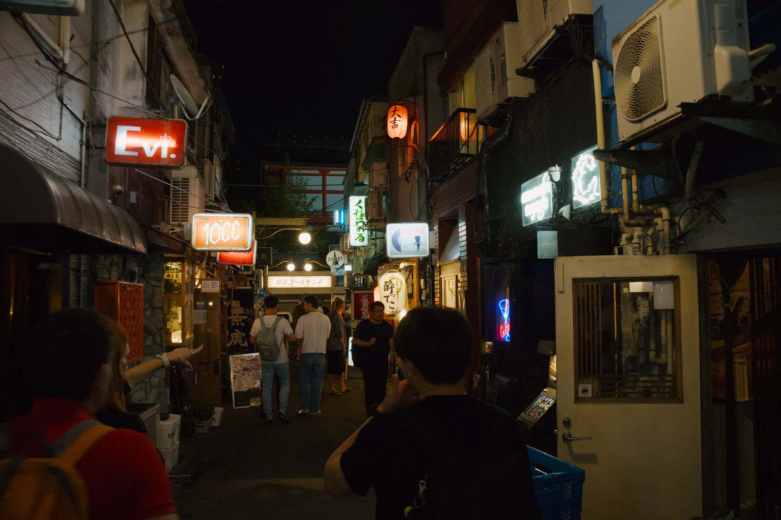 Quiet nighttime side street with traditional lantern-style lighting and storefronts, sparsely populated compared to main shopping streets.