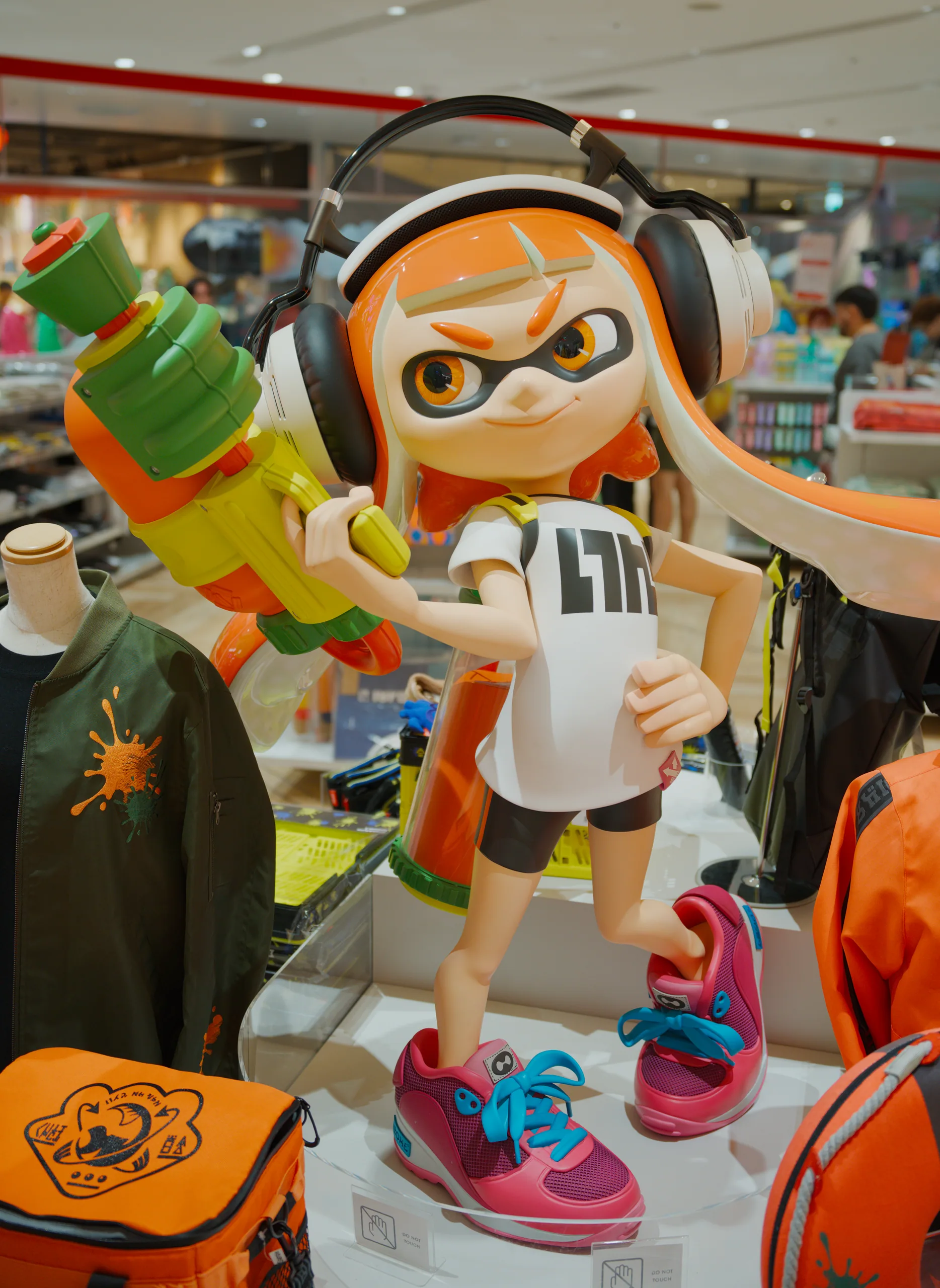 Inkling character figurine wearing headphones and orange clothing, surrounded by video game merchandise on display.
