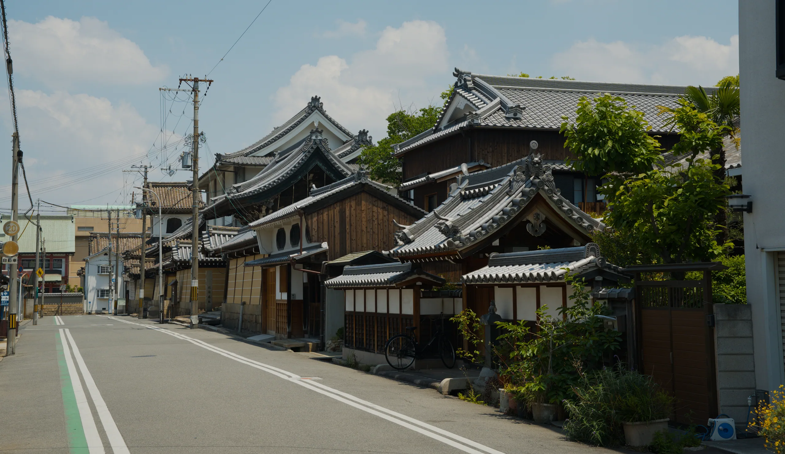 Traditional Japanese building with curved tile roof and wooden lattice walls on a street lined with utility poles.