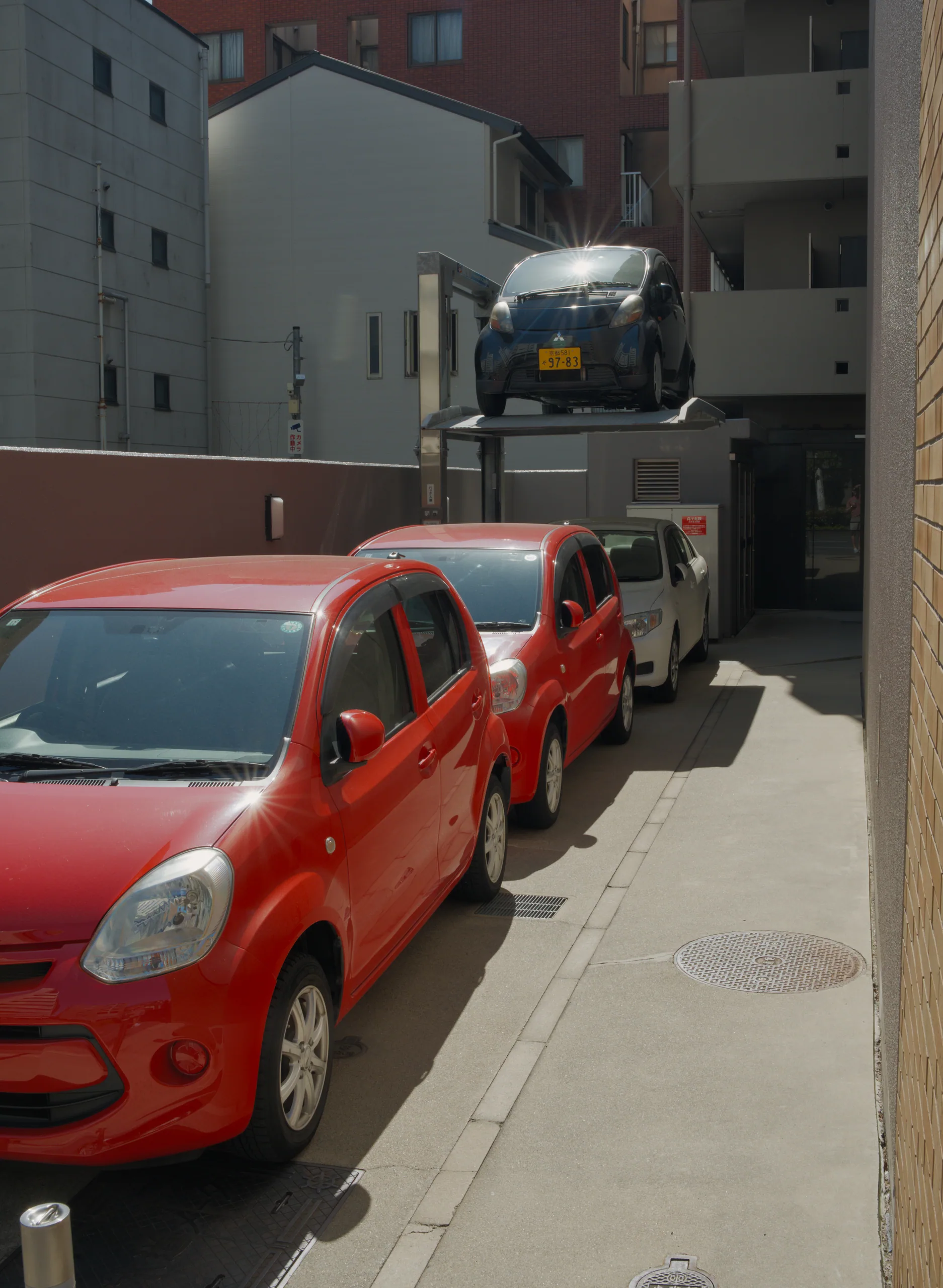 Red car parked on a narrow street lined with buildings in bright sunlight.