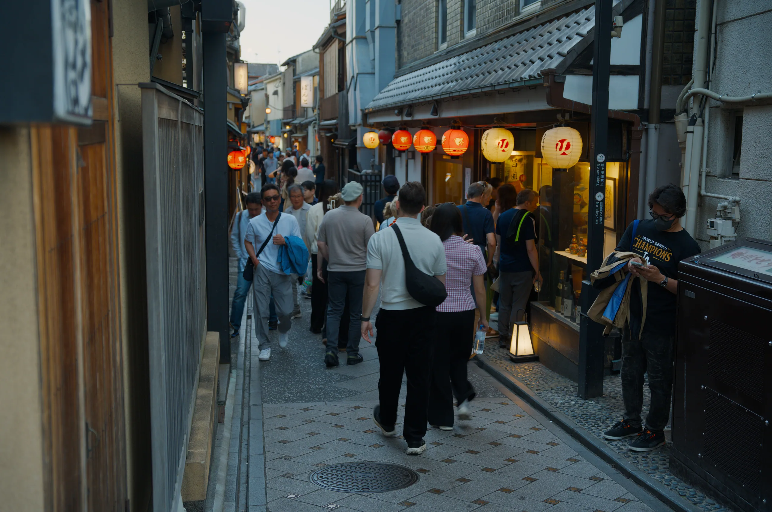 Half-timbered buildings and illuminated storefronts line a narrow European street filled with pedestrians.