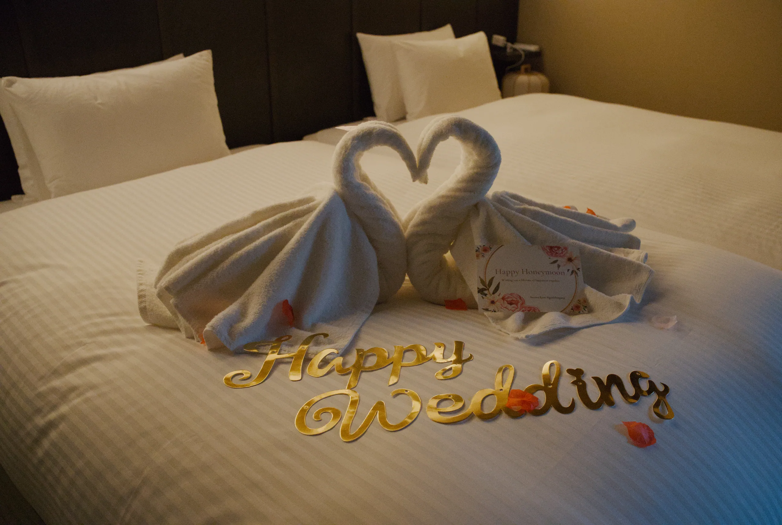 White pillows and cream bedding hold chocolate-covered strawberries arranged in a heart shape with 'happy wedding' written in chocolate.