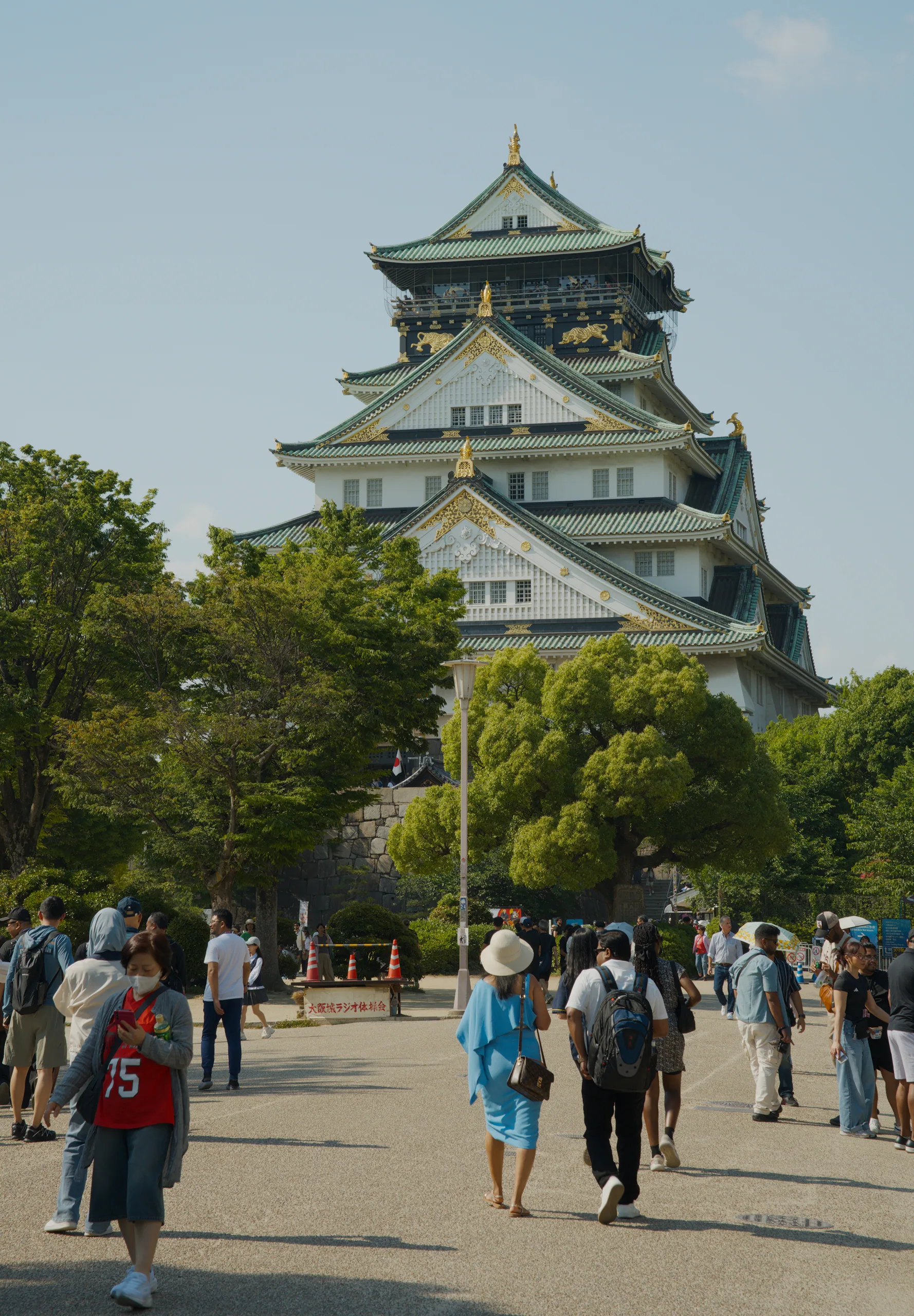 Multi-tiered Japanese castle with white and dark wooden structure and upturned roof edges, visitors on the plaza in front.
