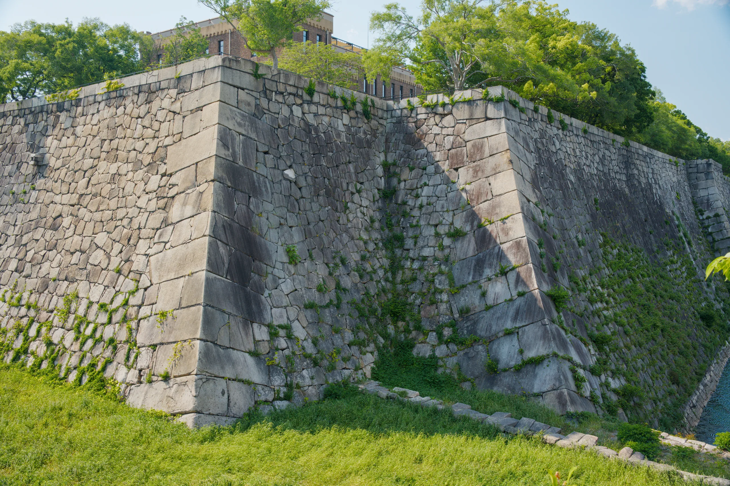 Angled stone fortification walls with weathered surface and moss-covered patches, grass area below.