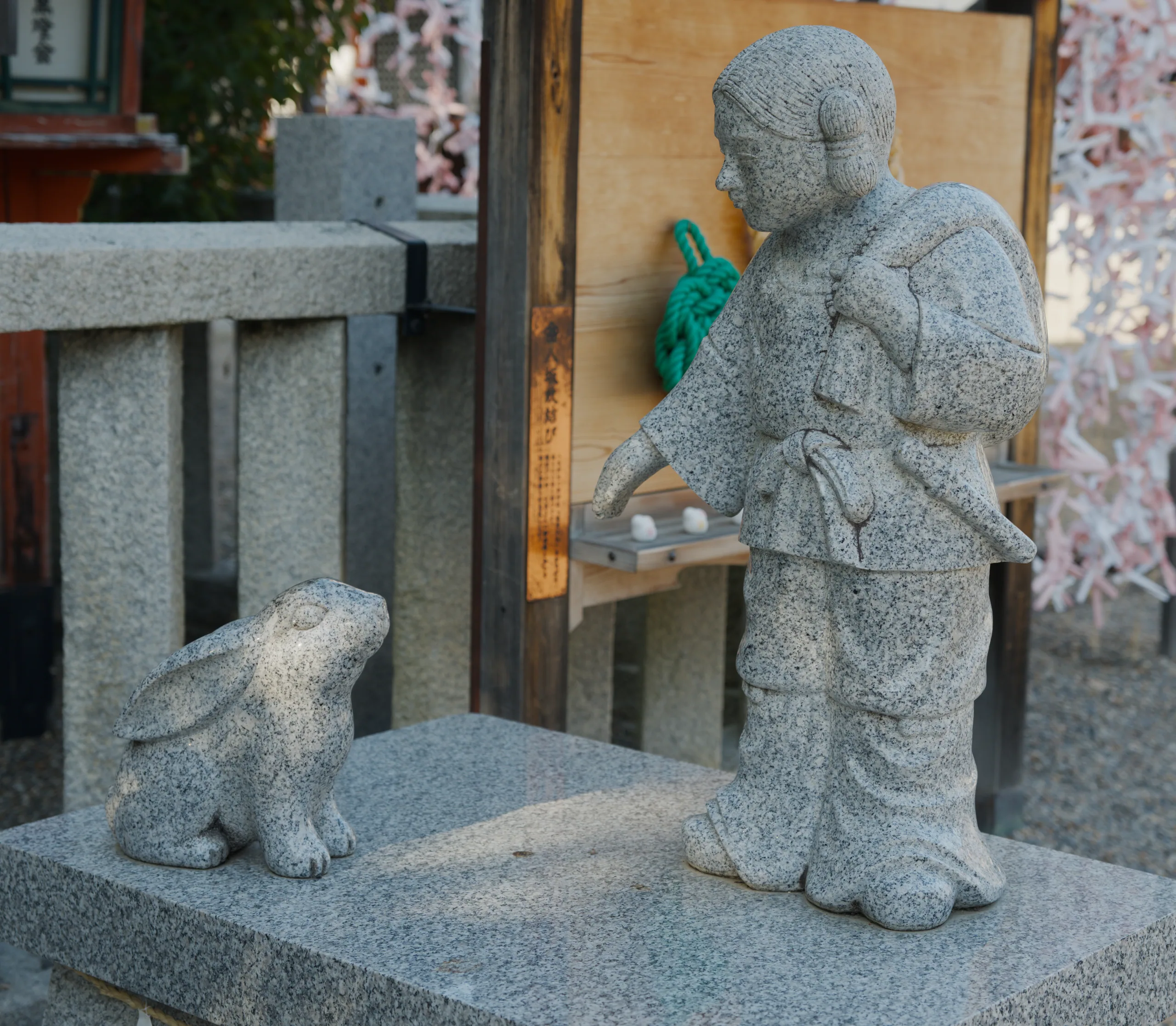 Two stone Buddhist figures seated on an altar beside a wooden structure.