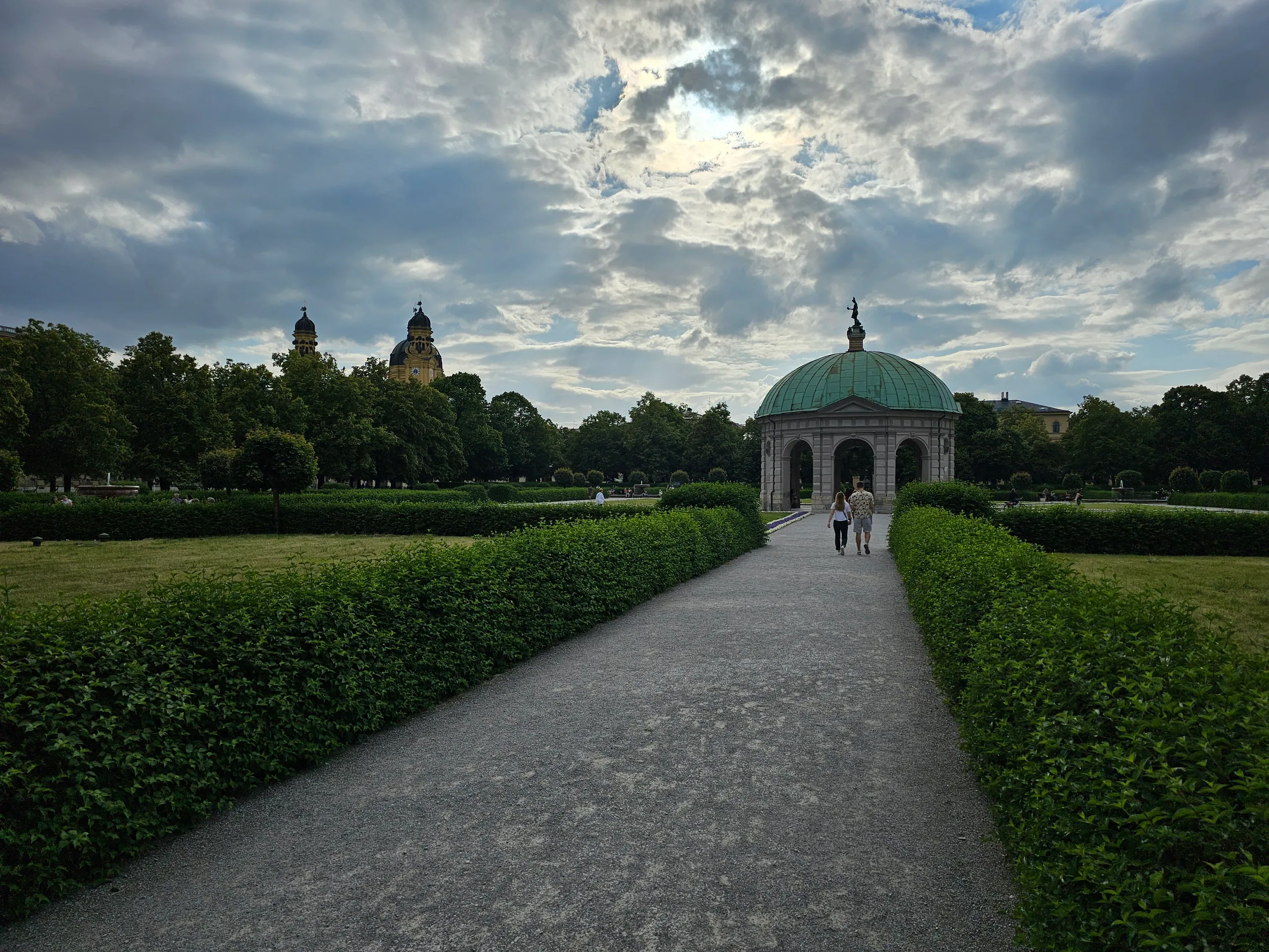A gravel path between low hedges running to the domed Diana temple in the Hofgarten under a heavy evening sky.