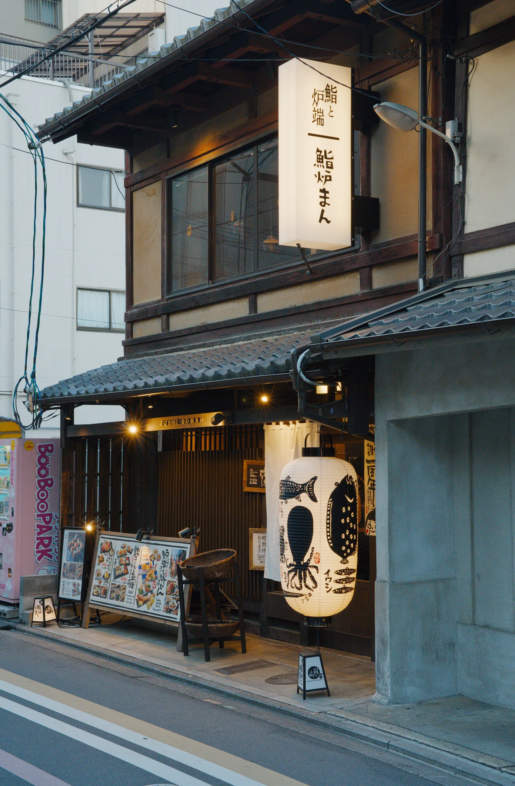 A traditional Japanese storefront with a white noren curtain bearing calligraphy and dark wooden framing.
