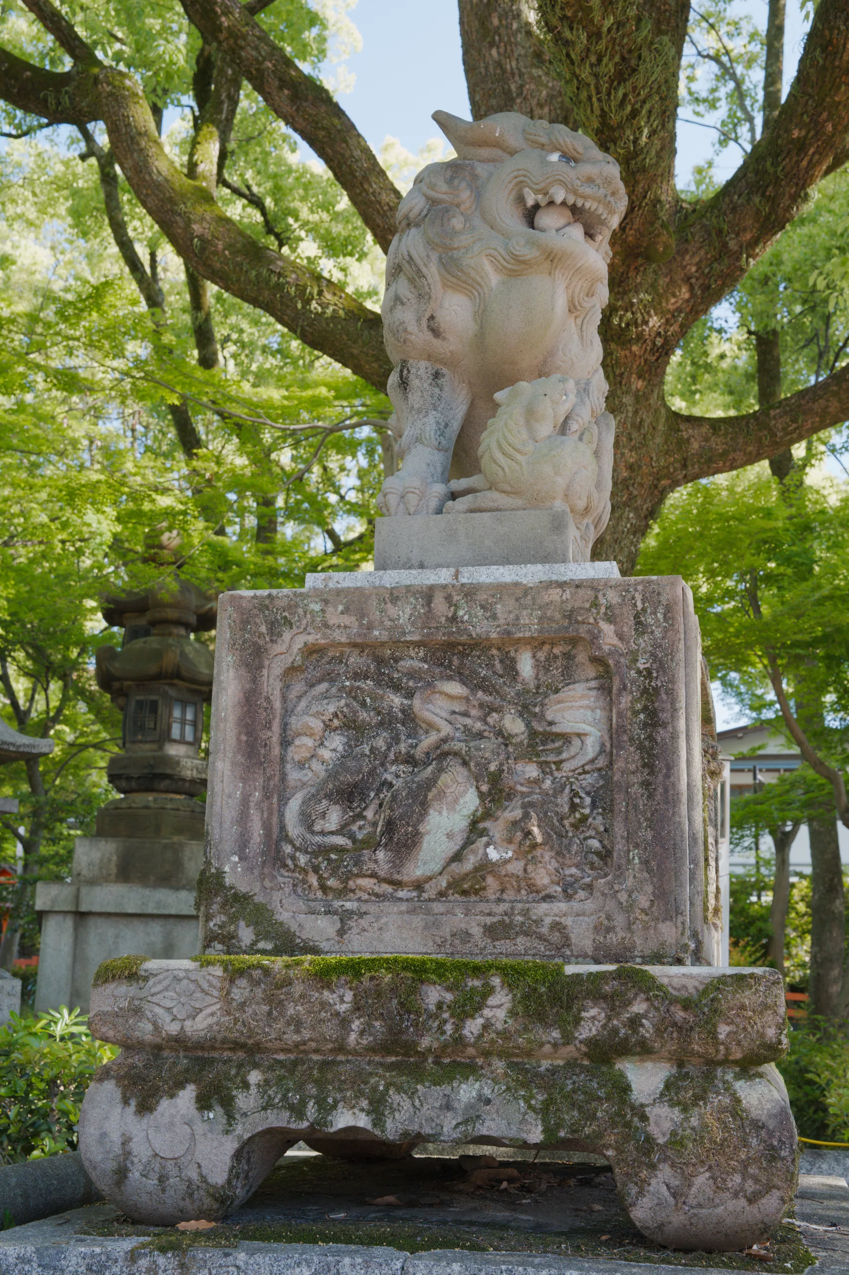 A stone guardian figure sits on a pedestal beneath spreading tree branches.