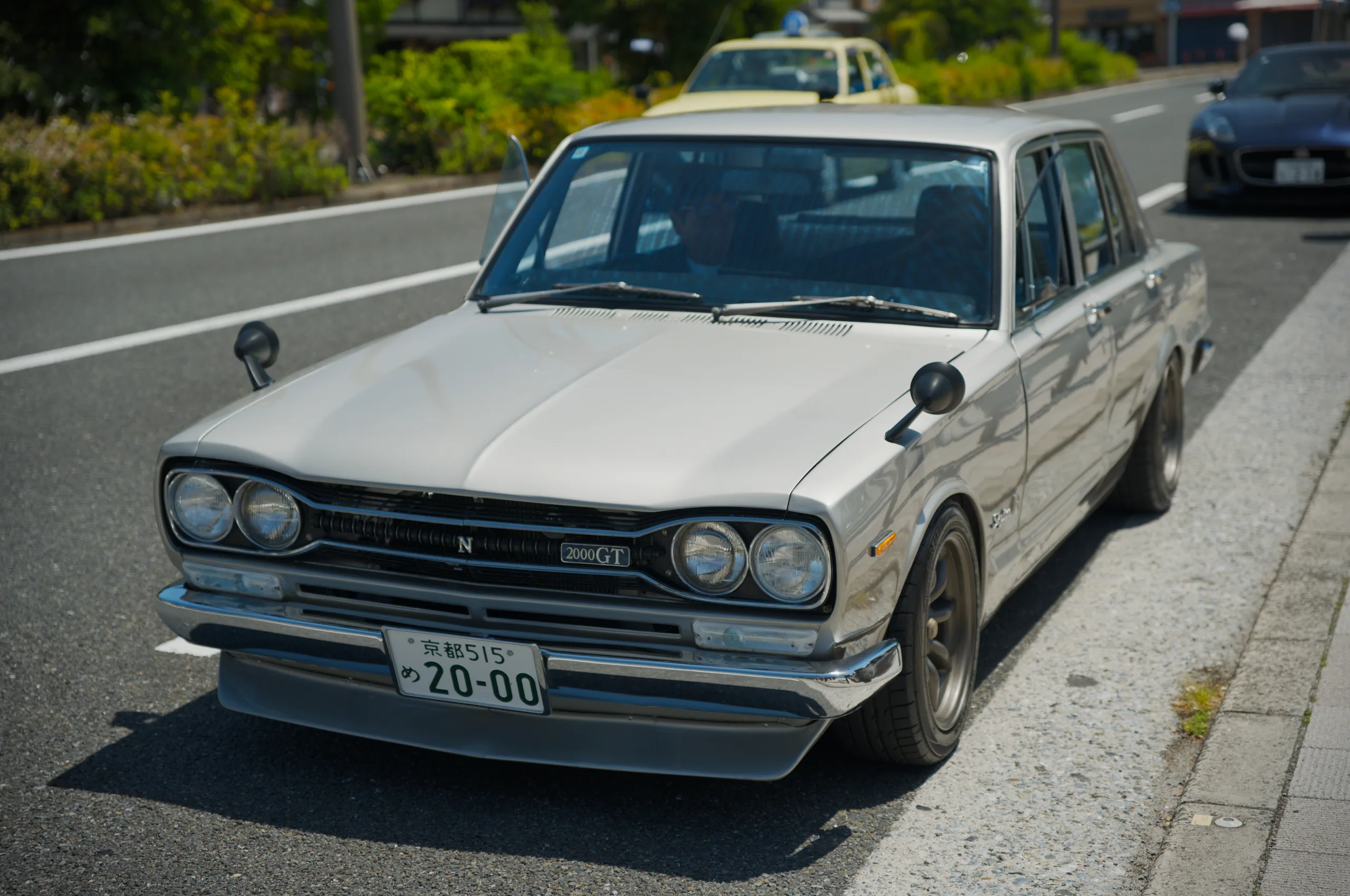 A vintage white sedan viewed from behind driving on a highway.