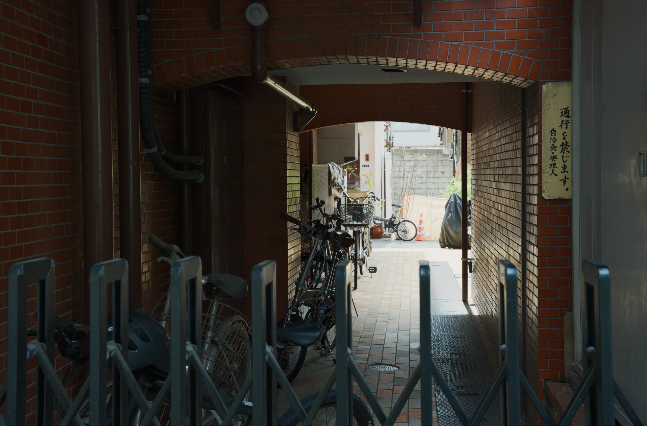 View through a covered entryway into a narrow alley with bicycles and traditional buildings.