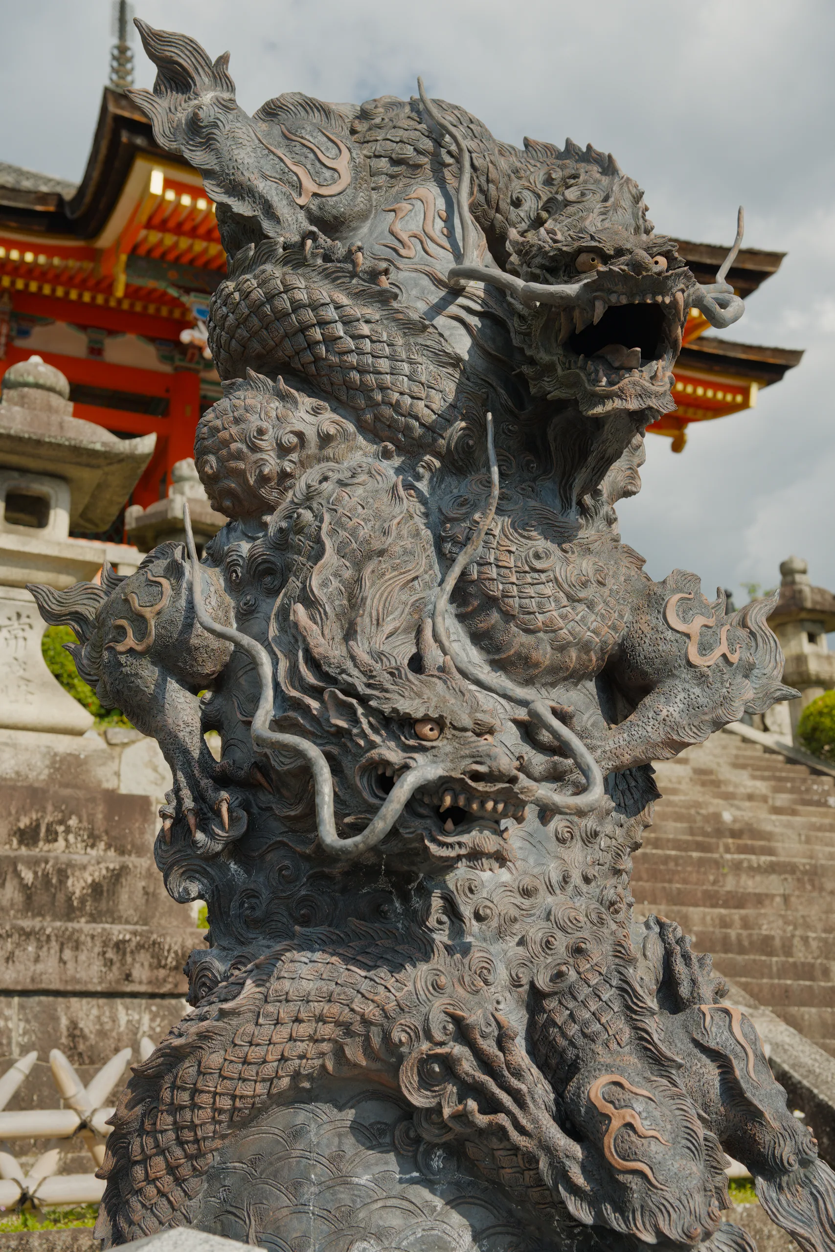 An ornate stone dragon guardian sculpture faces a temple with curved lacquered roofs.