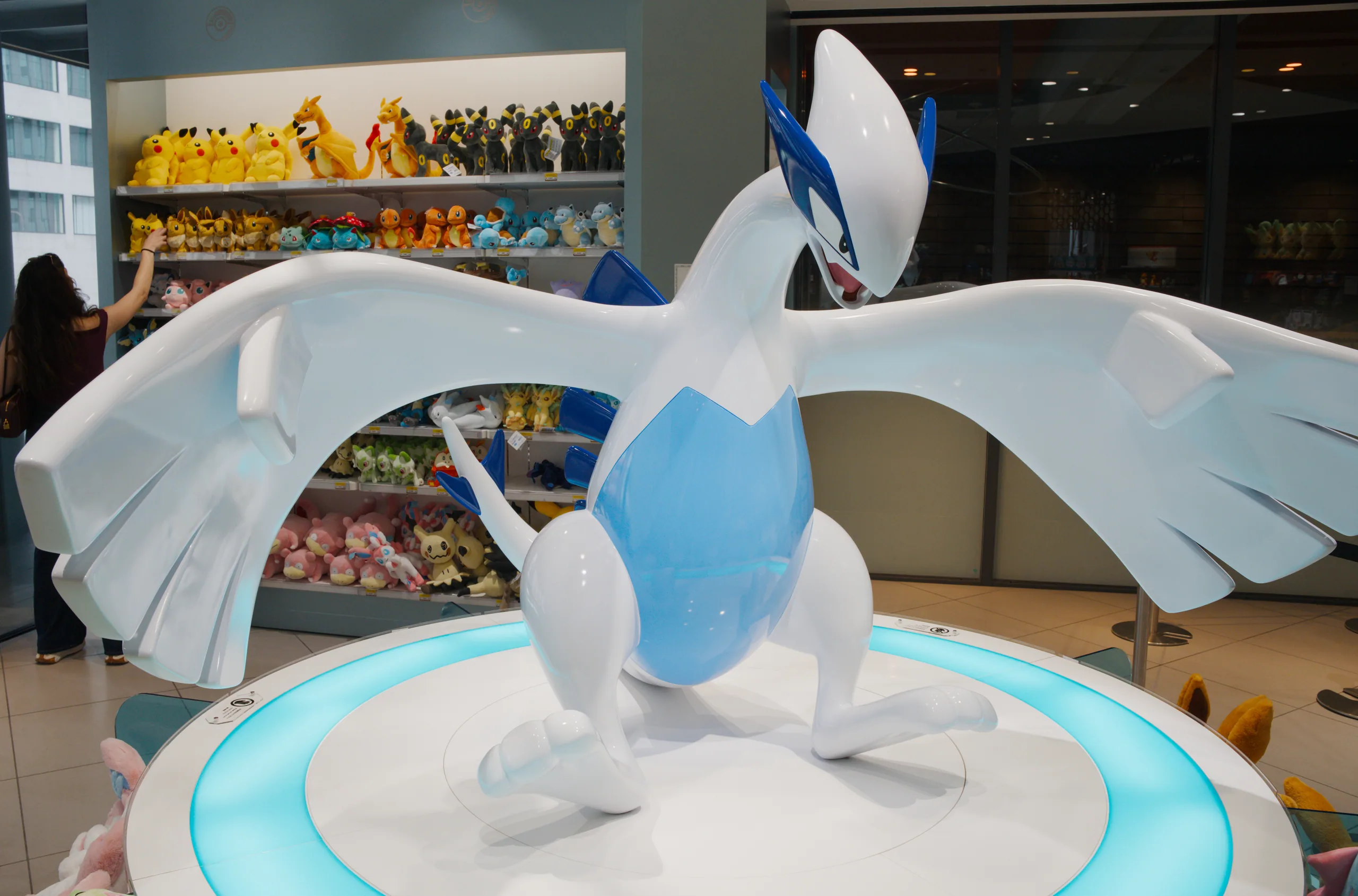 A white and blue Pokémon figurine stands on an illuminated turntable in a shop display.