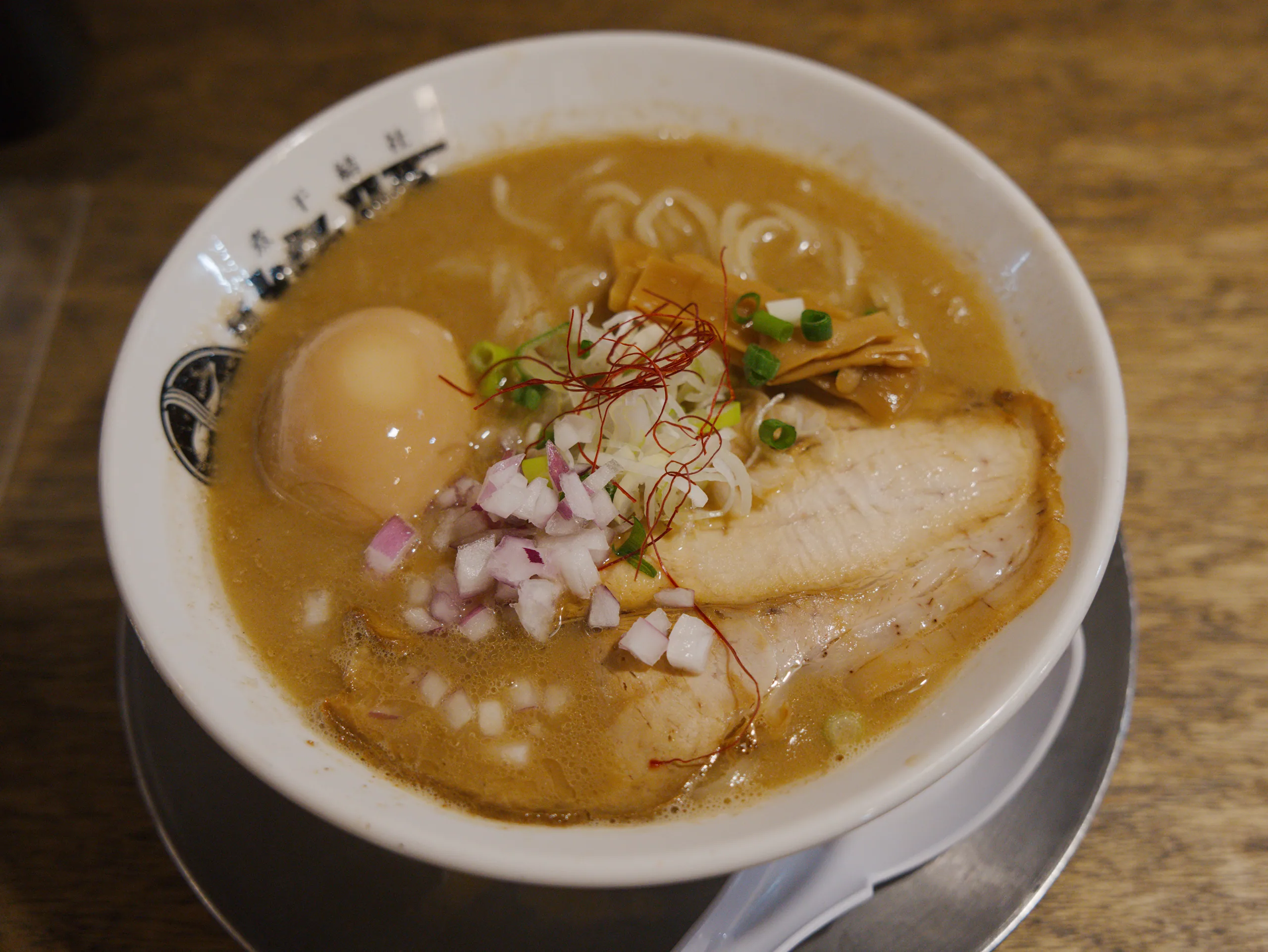 Ramen with golden broth, sliced pork, soft-boiled egg, pickled ginger, and crispy fried topping.