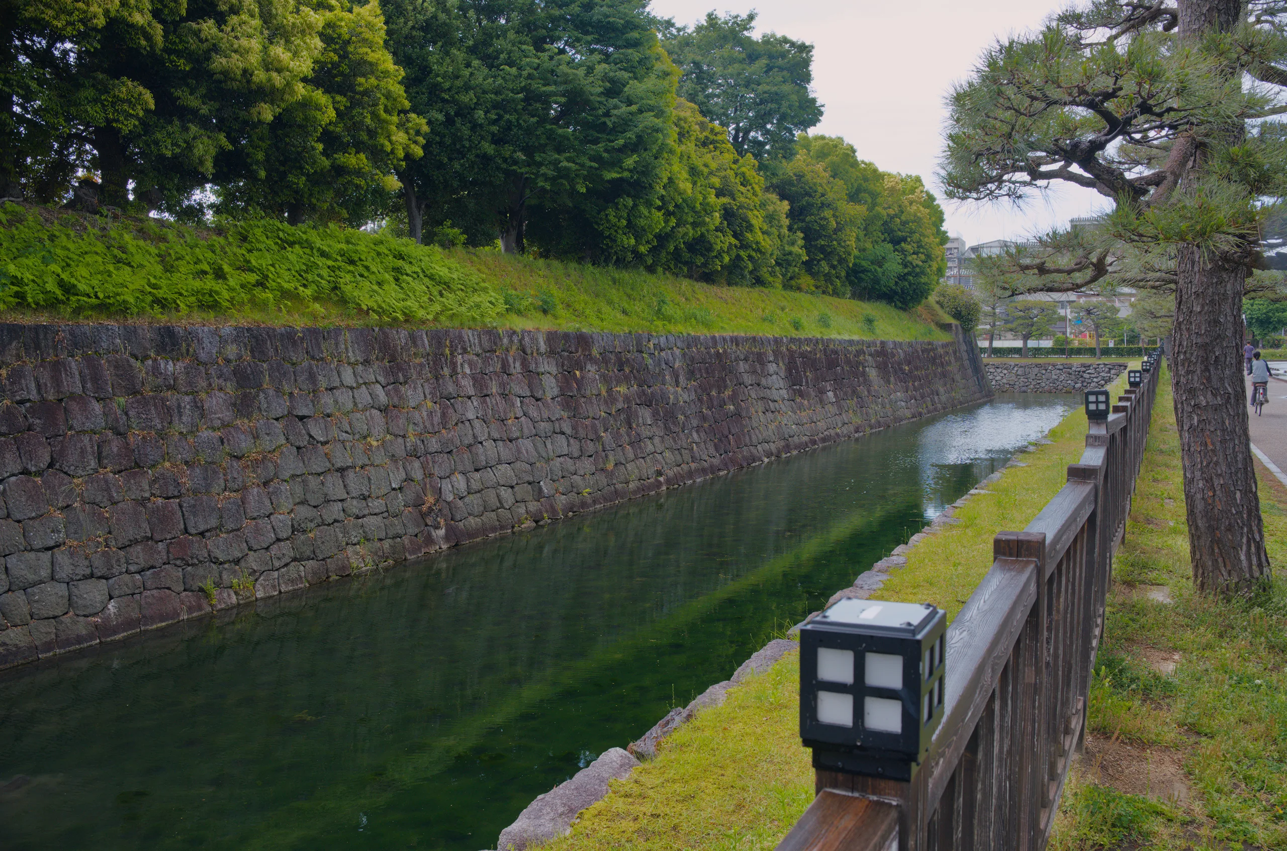 A substantial stone fortification wall runs along the grassy edge of a waterway.