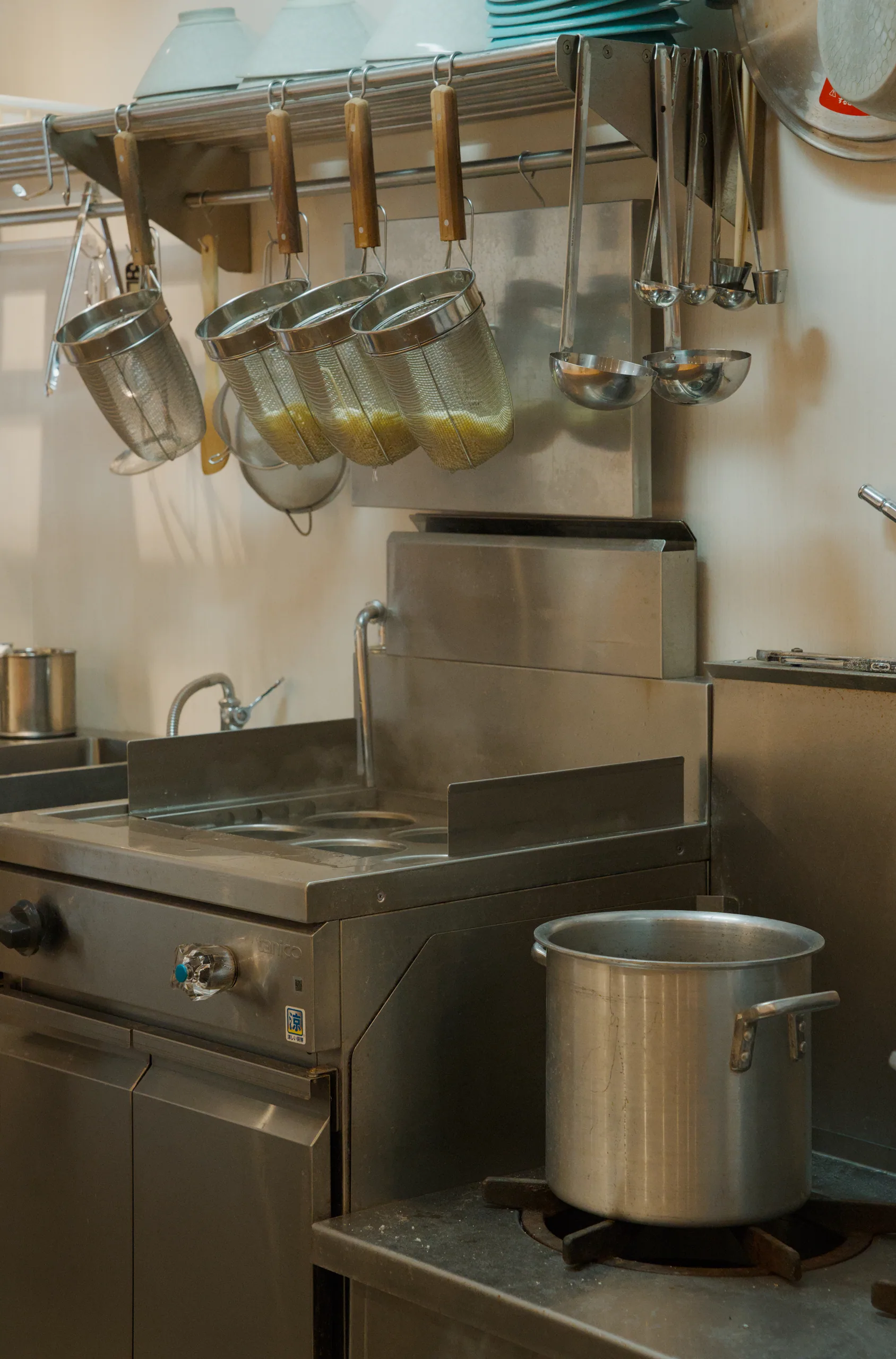 Hanging stainless steel pots and kitchen utensils on a shelf in professional kitchen.