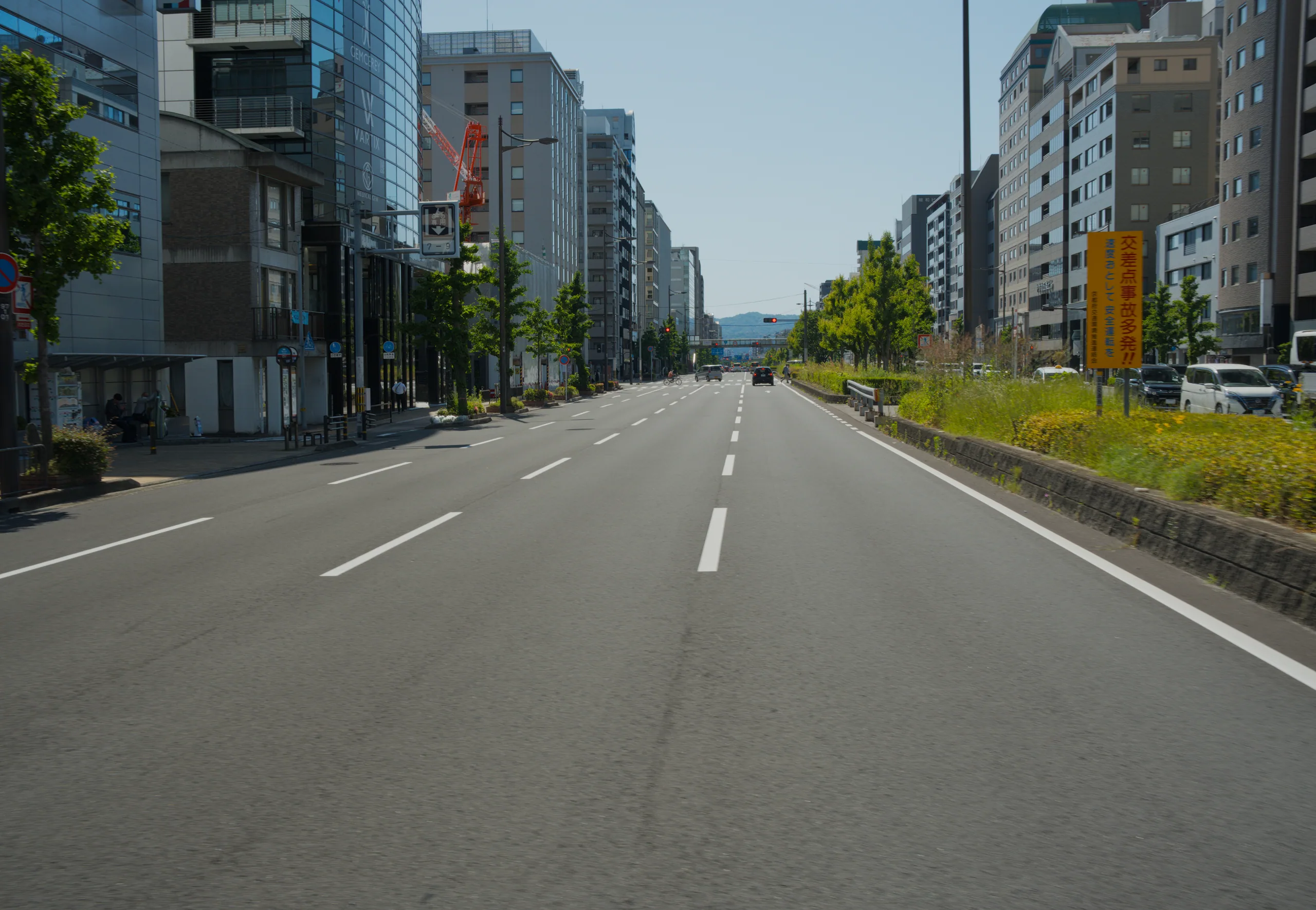 A broad urban avenue lined with tall buildings and green trees, with a river running alongside.
