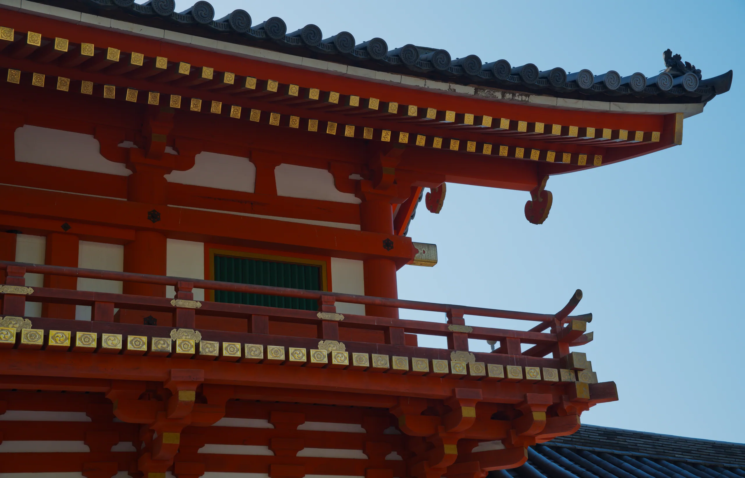 A red-painted Japanese pagoda structure with ornate eaves photographed from below against blue sky.