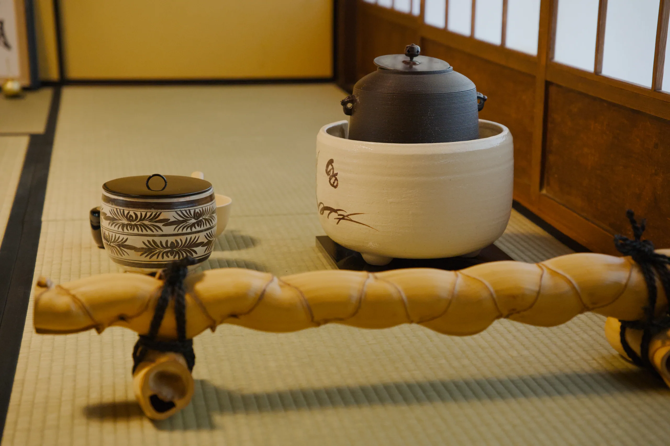 Tea ceremony utensils on tatami matting including a ceramic teapot, tea bowl, and bamboo whisk.