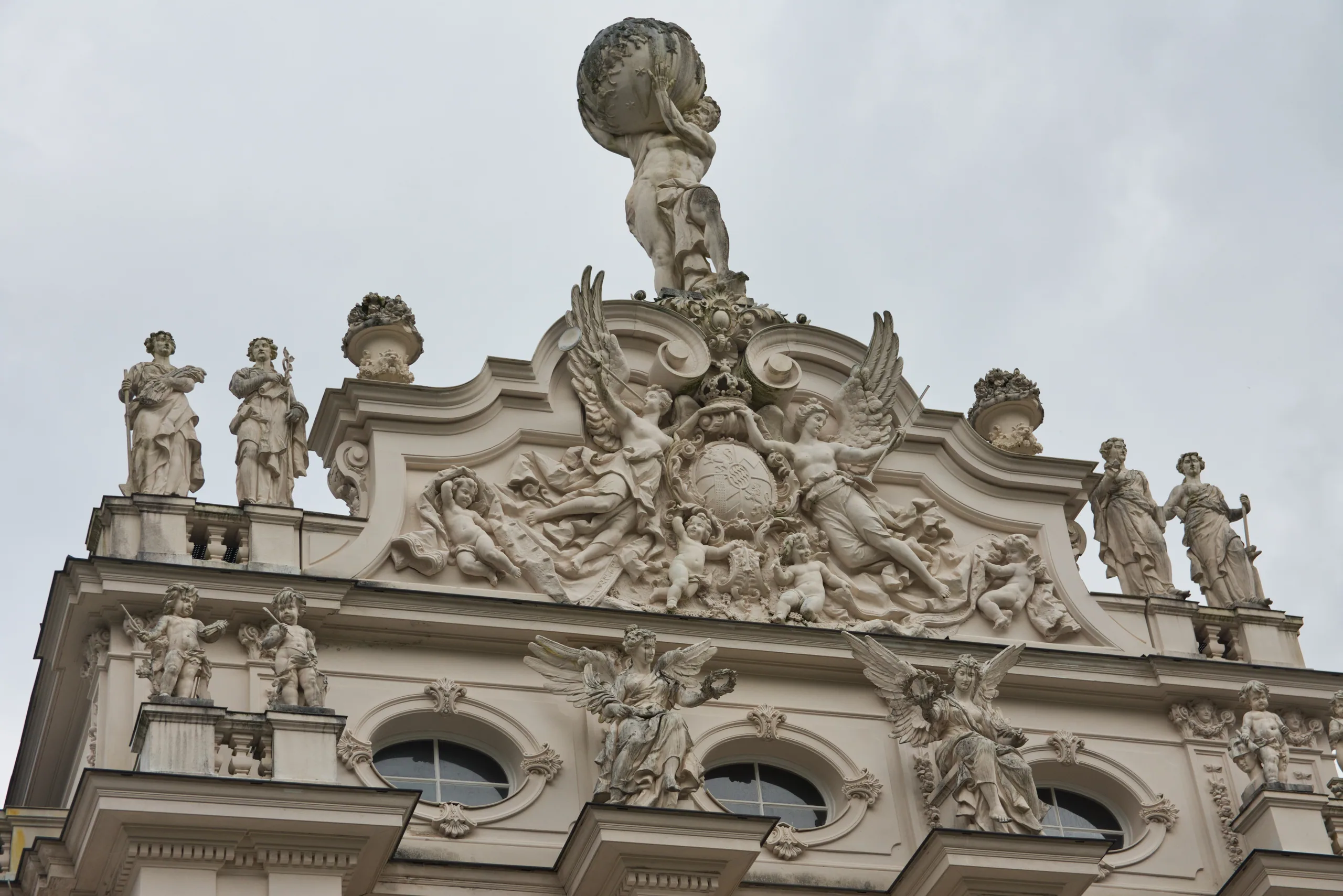 The sculpted baroque gable of a church, saints and cherubs standing along the parapet against a pale sky.