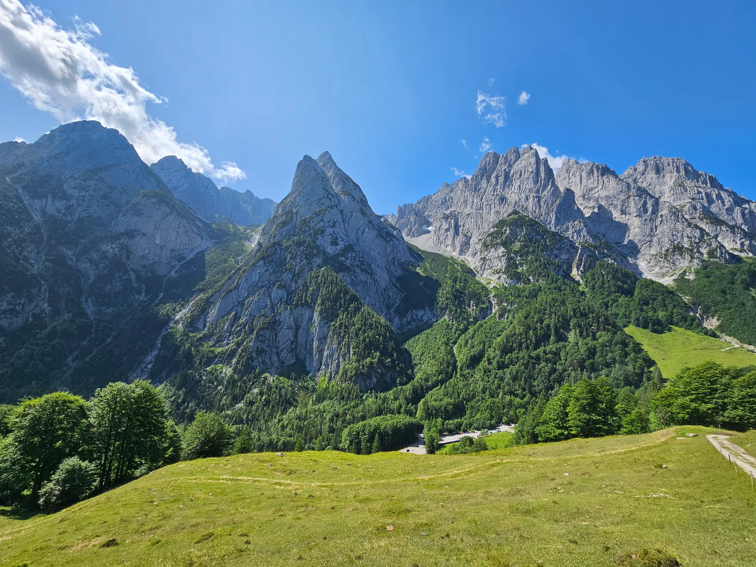 Grey limestone peaks above a green alpine pasture, a path running along the slope in the foreground.