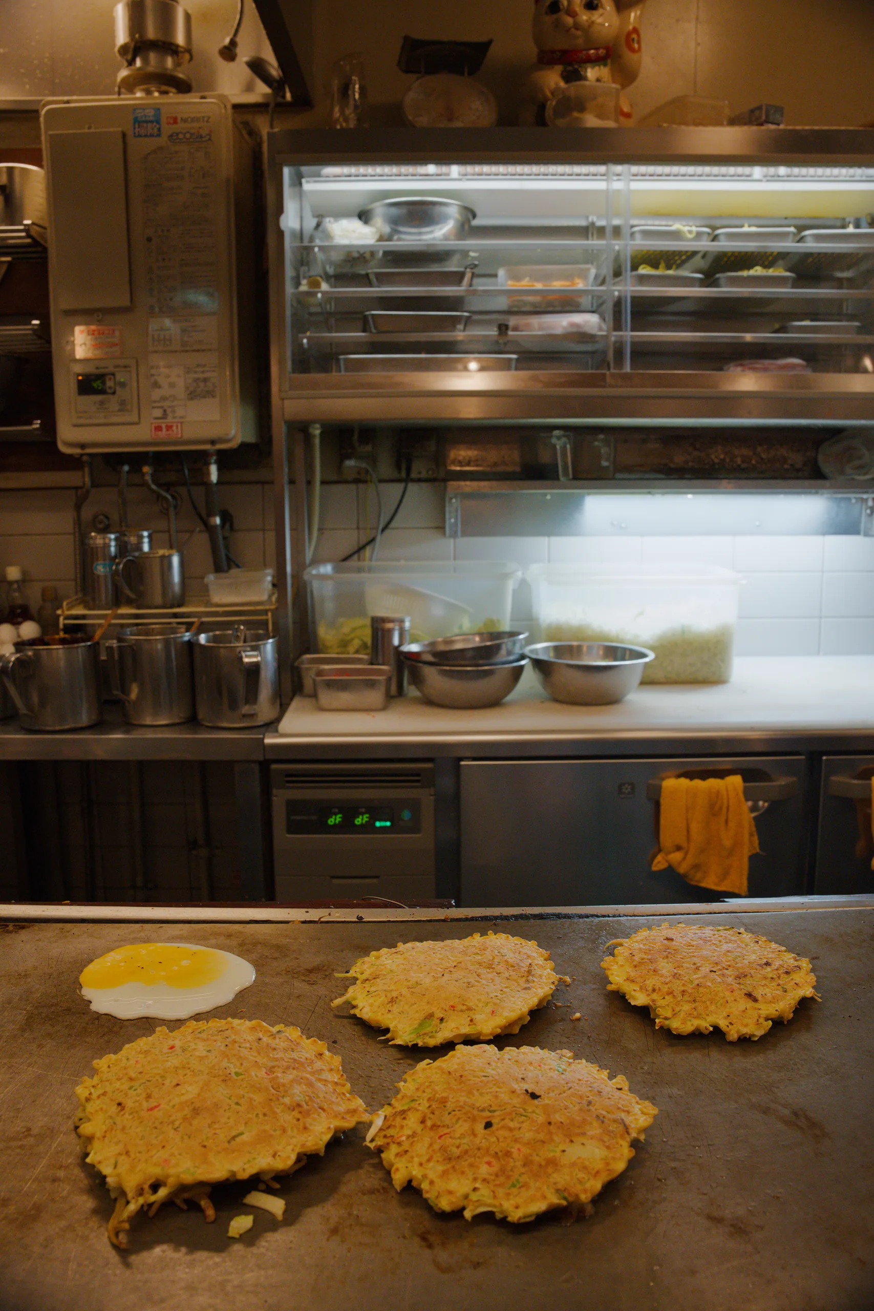 A restaurant kitchen at night with okonomiyaki cooking on a griddle.